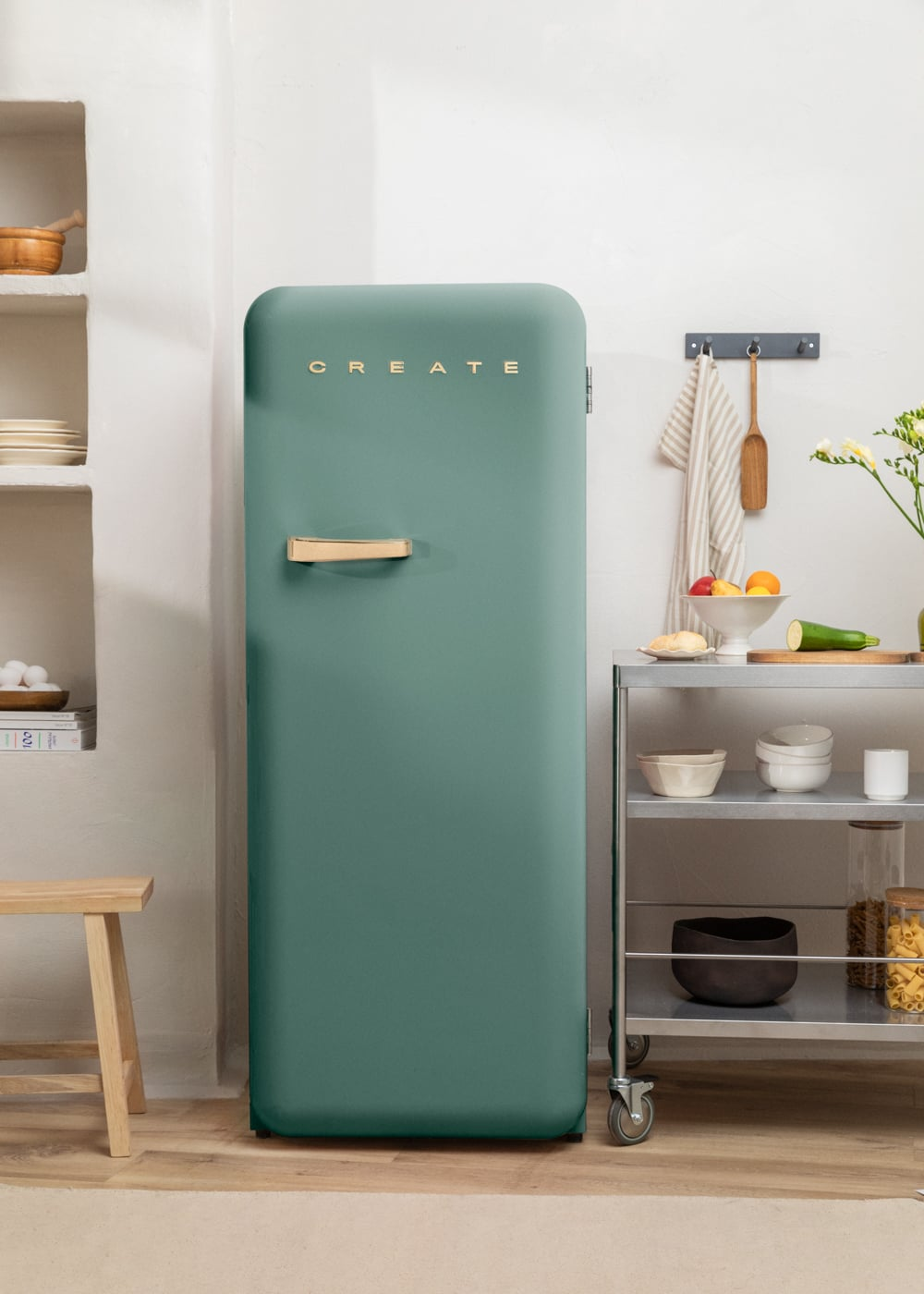 Un refrigerador verde esmeralda con asa dorada junto a un carrito de cocina.
