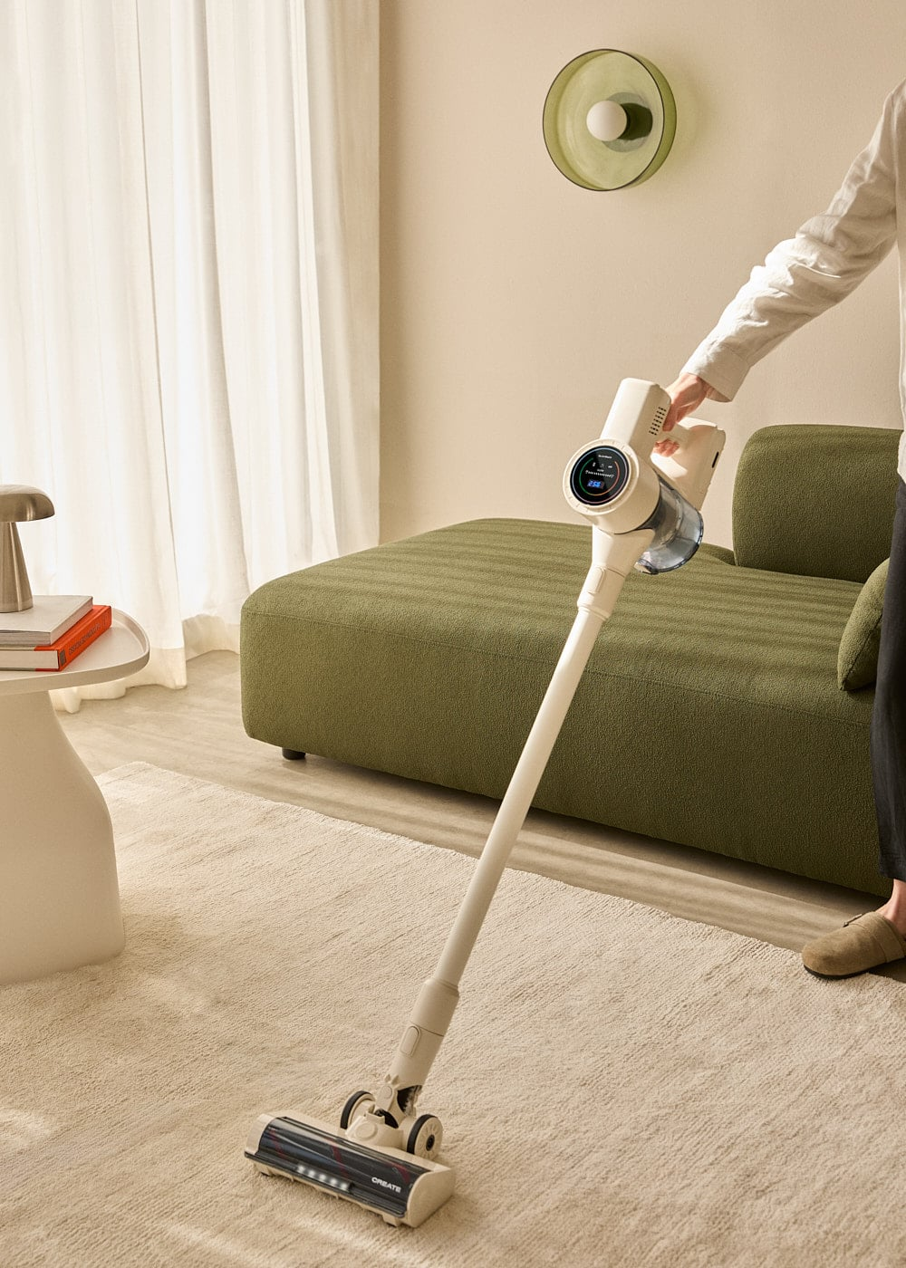 Una persona aspira una alfombra beige claro con una aspiradora blanca de palo en una habitación moderna.