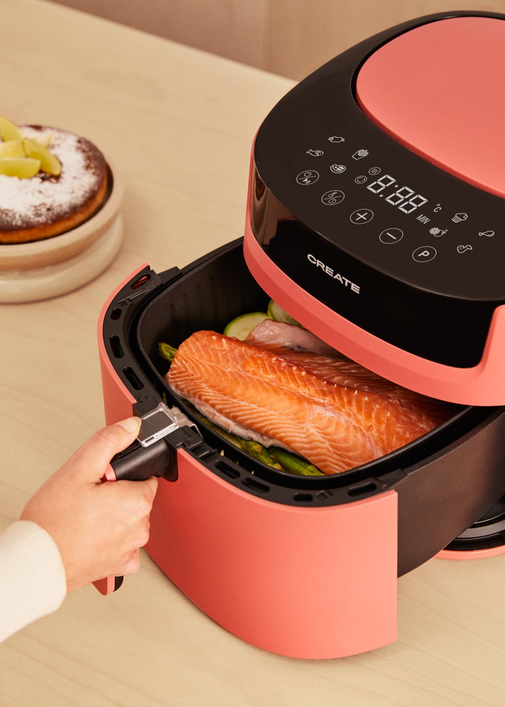 Una persona mette salmone e verdure in una friggitrice ad aria rosa.