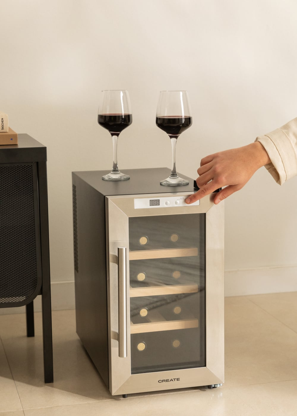 Un enfriador de vino con dos copas de vino tinto y una mano presionando un botón.