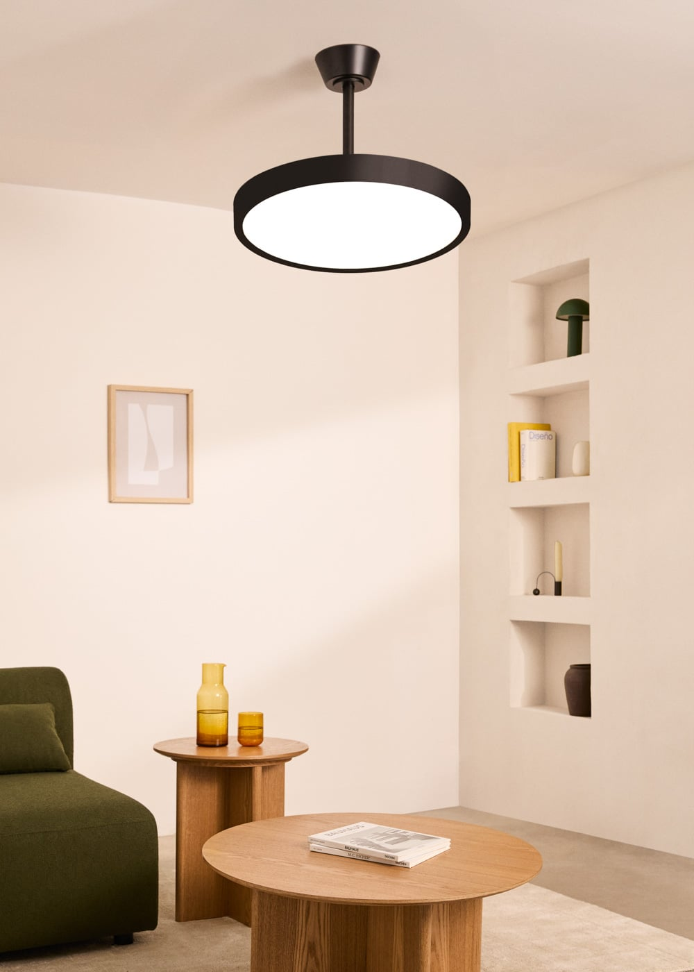 Un ventilador de techo negro con luz sobre una mesa de madera con libros y un sofá verde.