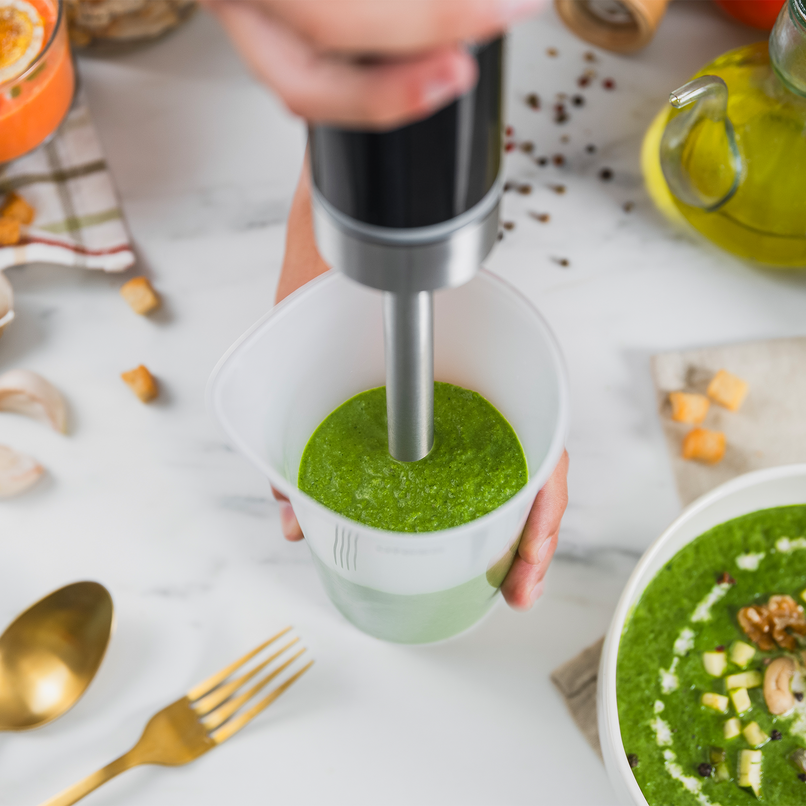 Sopa verde siendo licuada con batidora de mano, con ingredientes cerca.