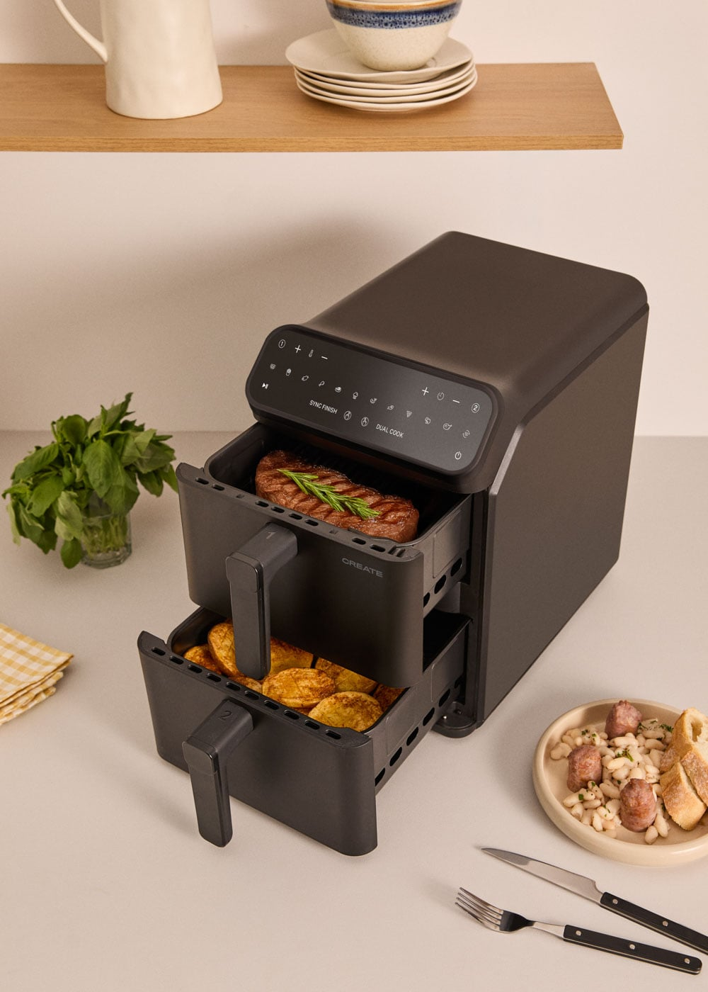 Freidora negra de doble cesta con bistec en la cesta superior, patatas fritas abajo.