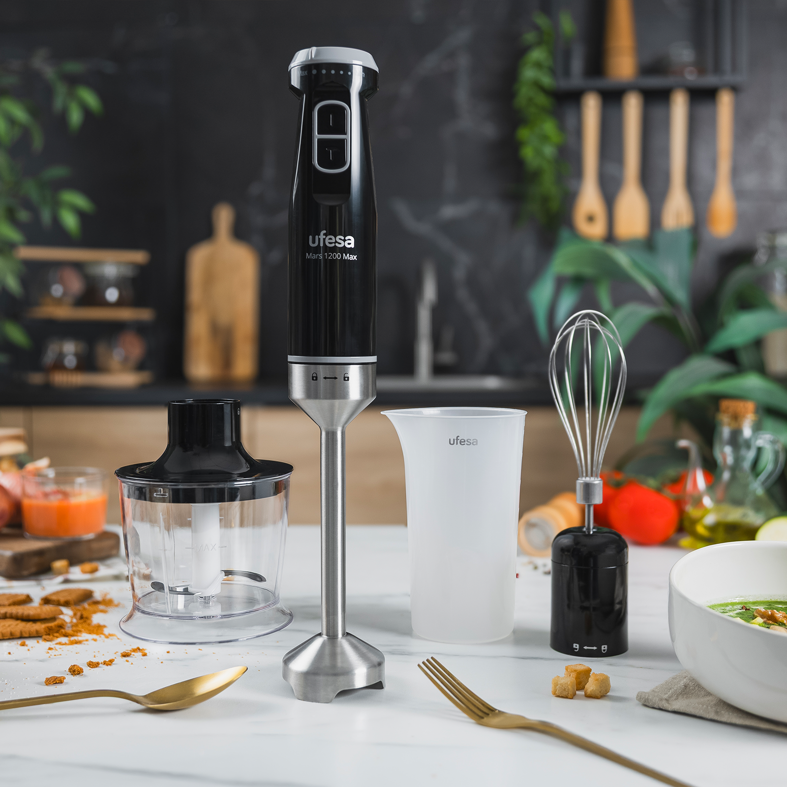 Un frullatore a immersione nero con accessori su un tavolo di marmo, cucina sullo sfondo.