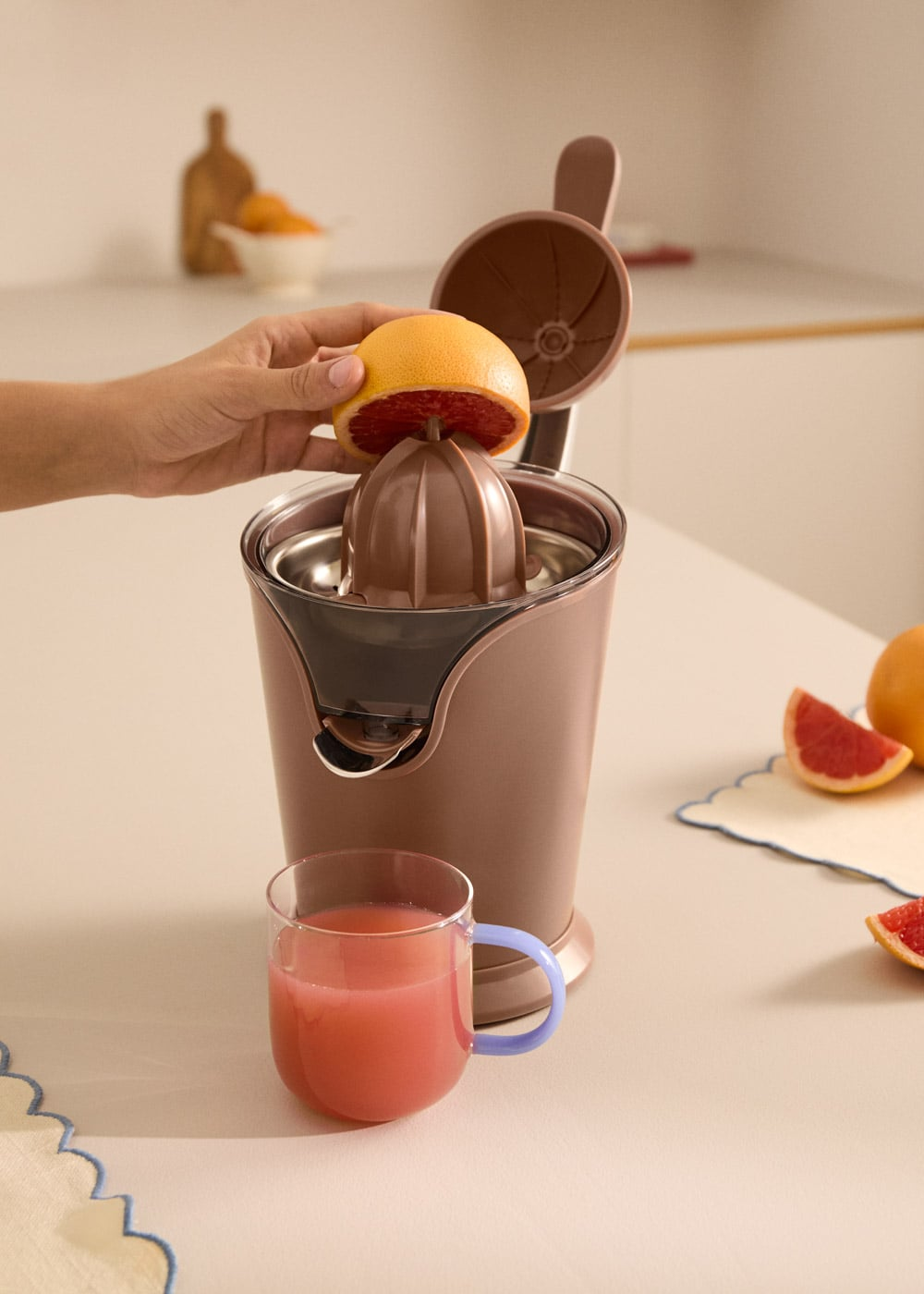 Una mano exprime una toronja en un exprimidor. Un vaso de jugo está cerca.