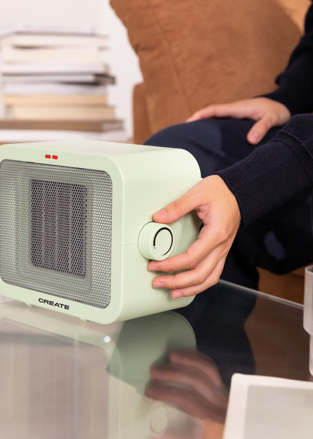 Una persona ajusta el dial de un calefactor verde claro sobre una mesa de cristal.