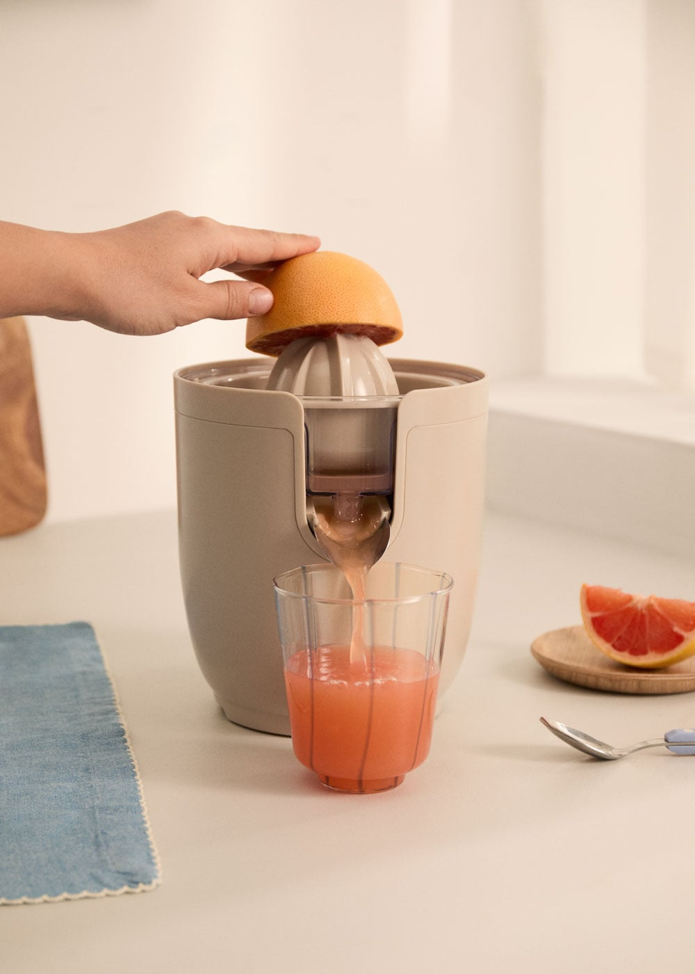 Una mano presiona una toronja sobre un exprimidor, el jugo fluye hacia un vaso.