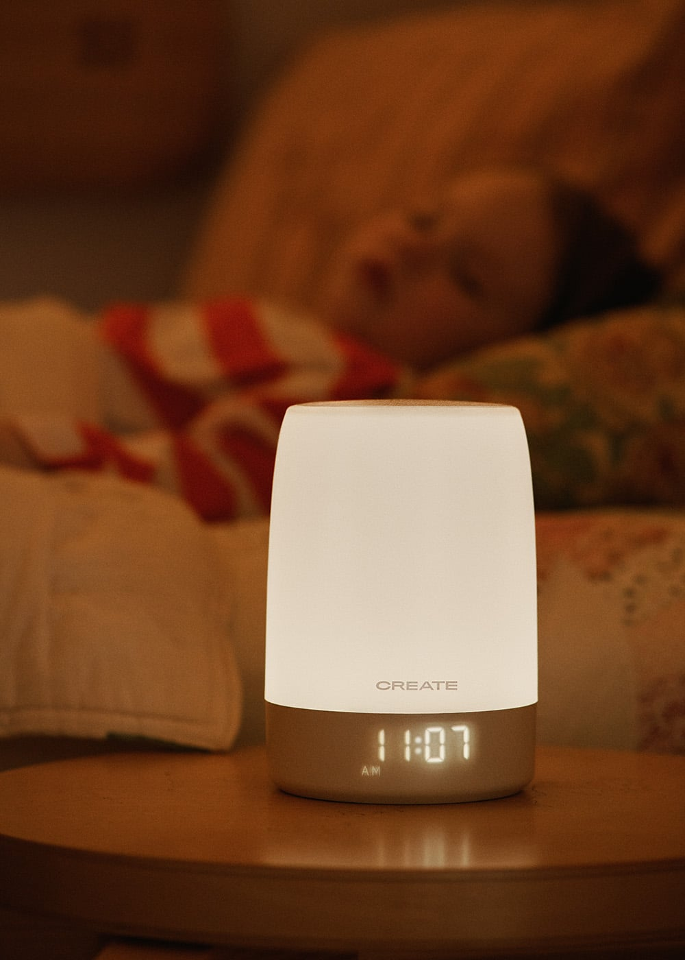 Una lámpara blanca con reloj digital (11:07 AM) delante de un niño durmiendo.