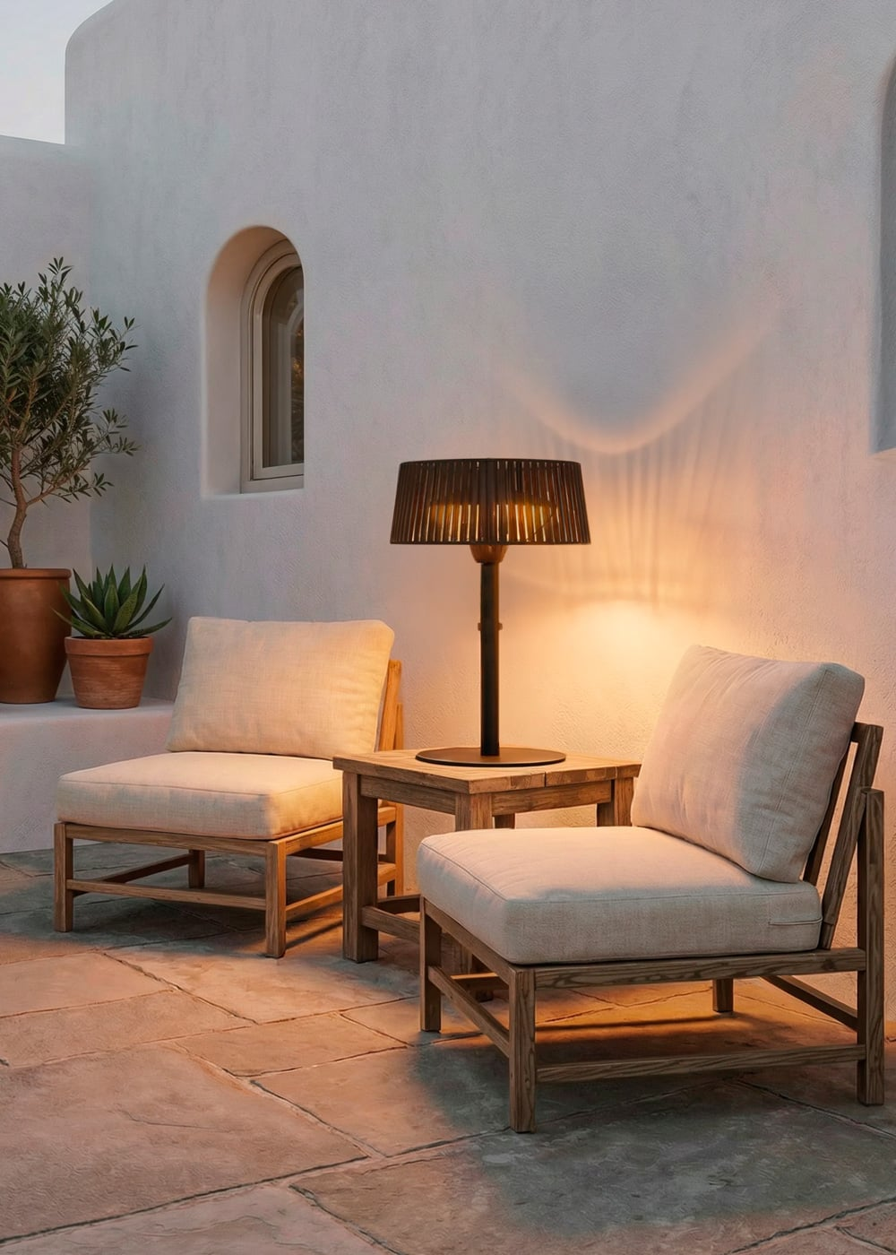 Dos sillas claras y una mesa auxiliar con lámpara en un patio de piedra.