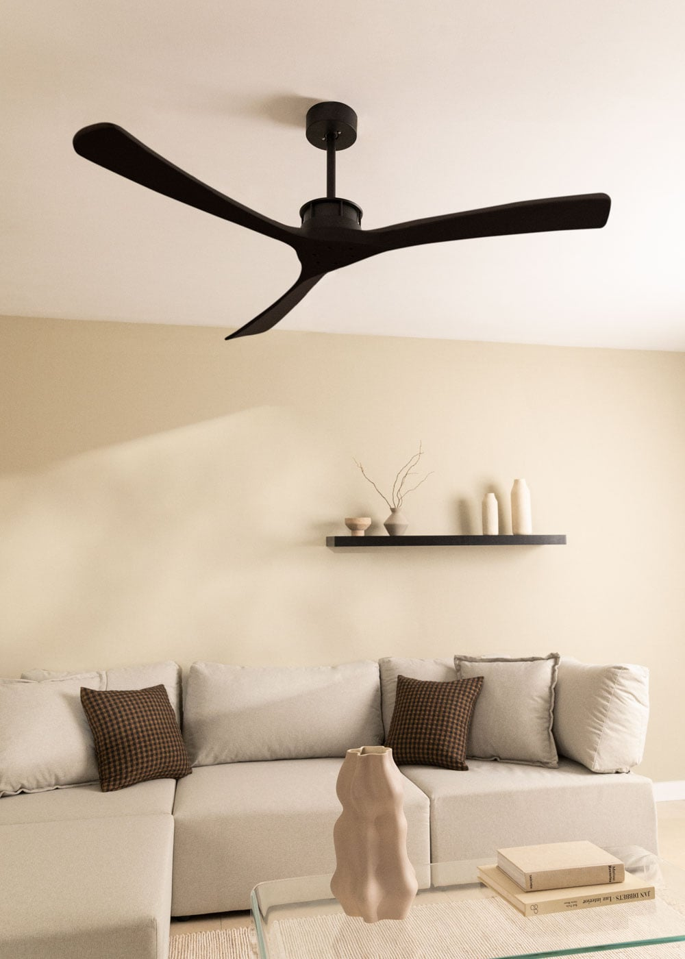 Un ventilador de techo negro sobre un sofá modular beige con cojines y una mesa de centro de cristal.