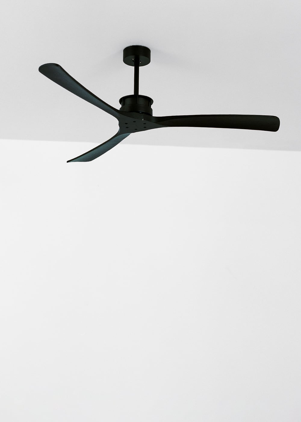 Un ventilador de techo negro con tres aspas cuelga de un techo blanco.