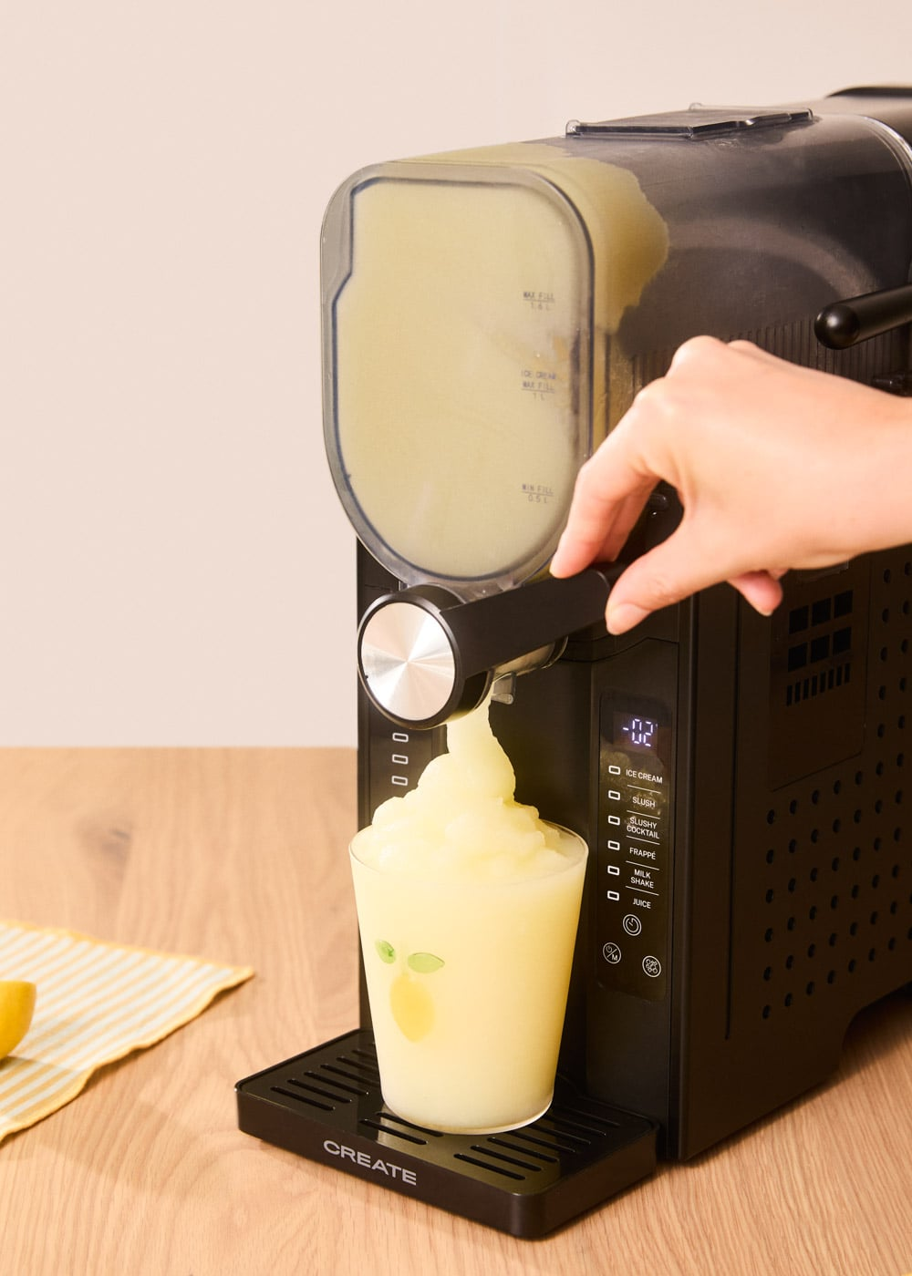 Una mano opera una máquina de granizados, sirviendo granizado amarillo en un vaso.