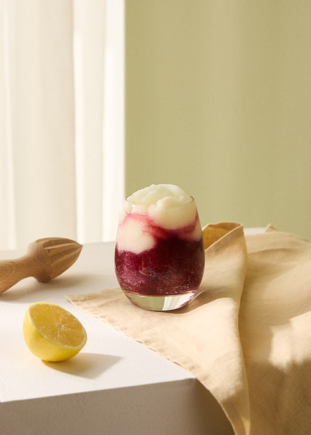 Bebida congelada en capas roja y blanca en vaso, limón y exprimidor.