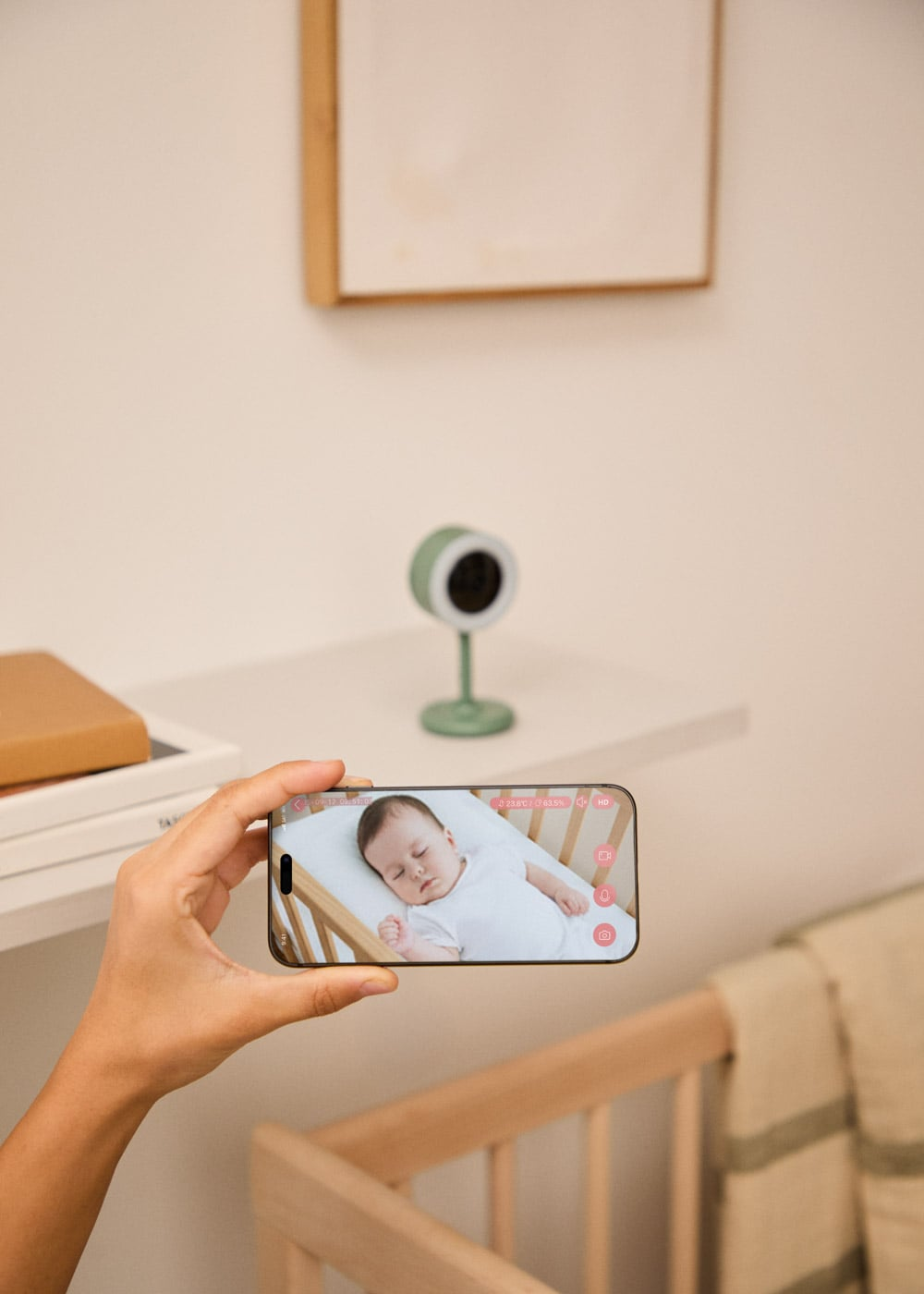 Un smartphone muestra un bebé durmiendo en una cuna, con una cámara de vigilancia de bebé detrás.