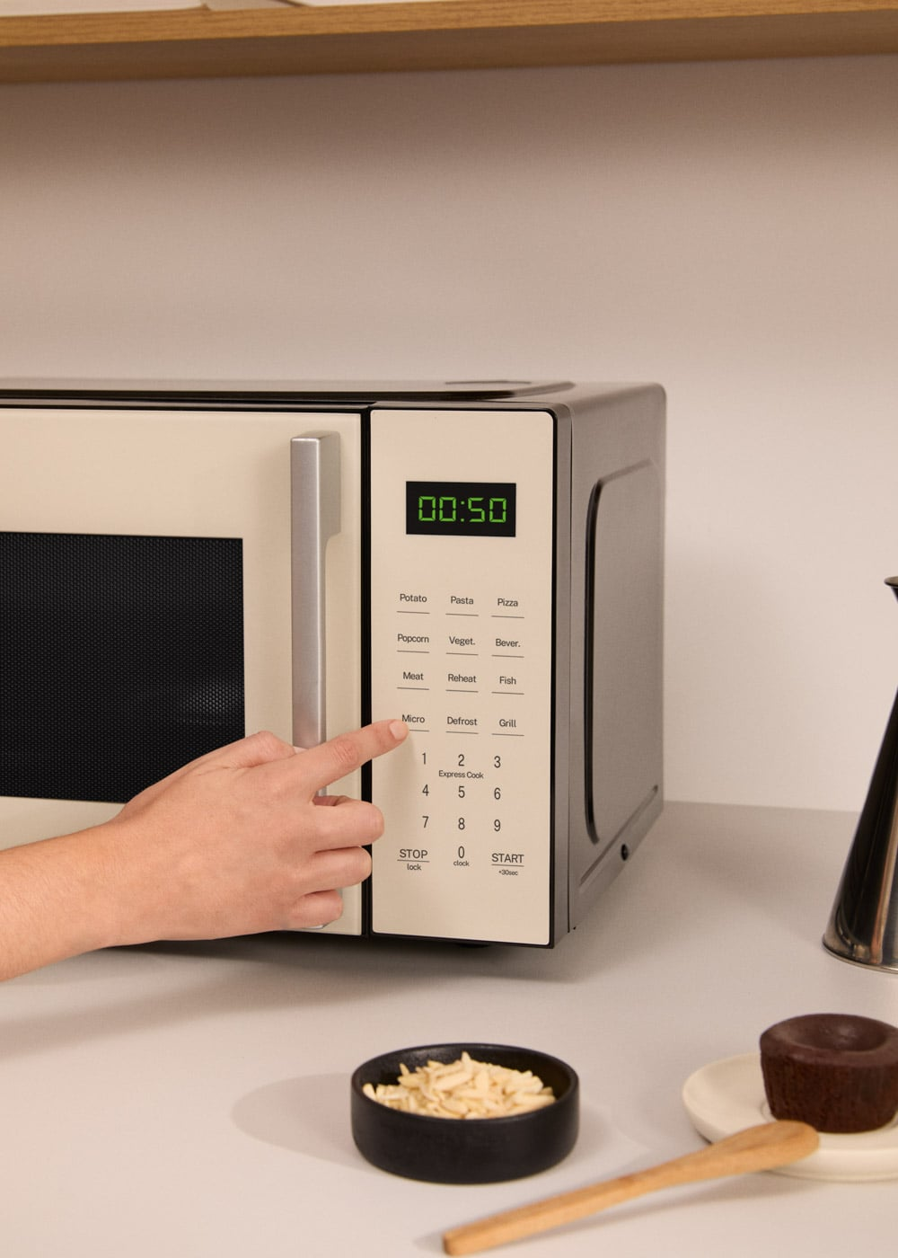 Una mano presiona el botón "Micro" en un microondas con 50 segundos mostrados.