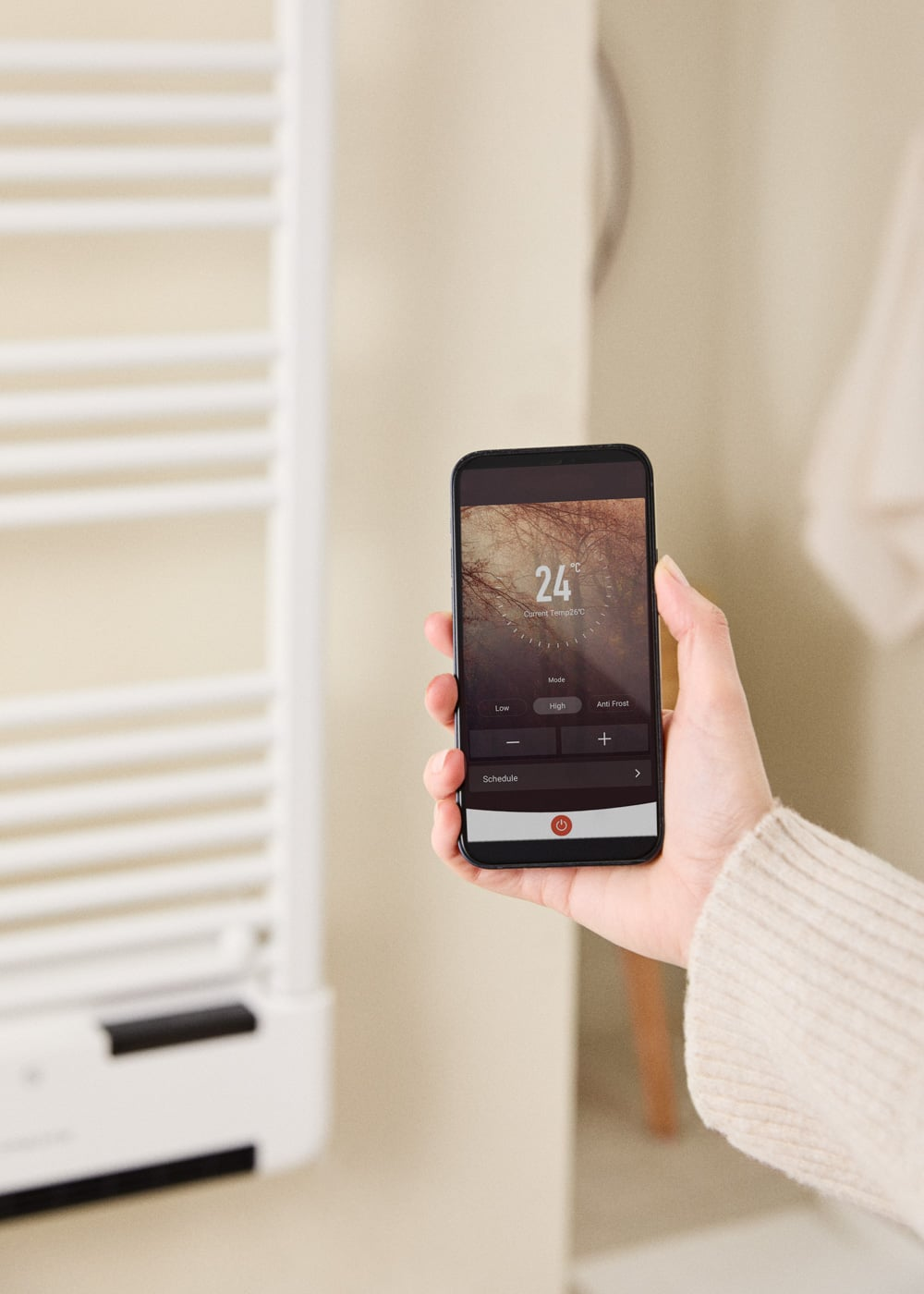 Una mano sujeta un smartphone con control de calefacción junto a un radiador.