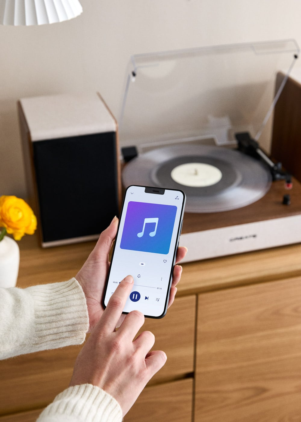 Persona operando smartphone con app de música frente a tocadiscos y altavoz.