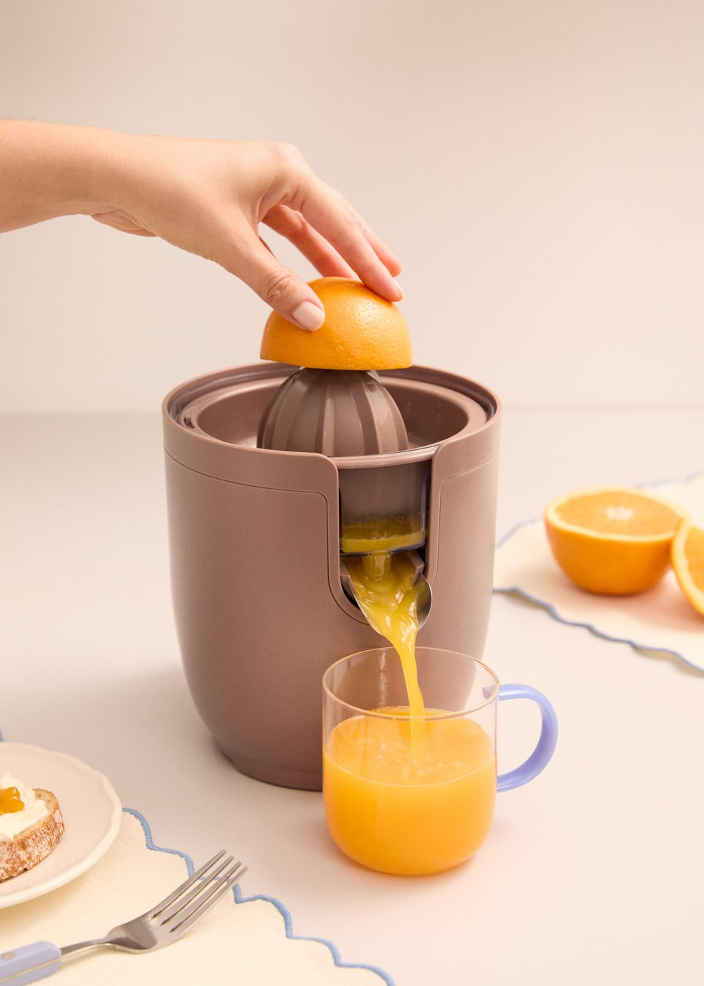 Una mano exprime una naranja en un exprimidor, el zumo fluye a un vaso.