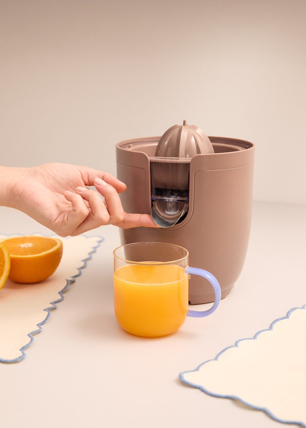 Una mano presiona un botón en un exprimidor junto a un vaso de jugo de naranja.
