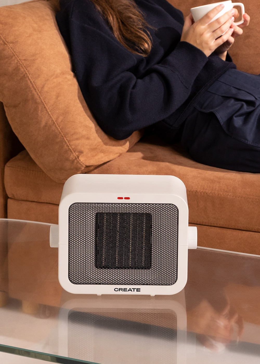 Un calefactor con ventilador blanco y rejilla está en una mesa de cristal.