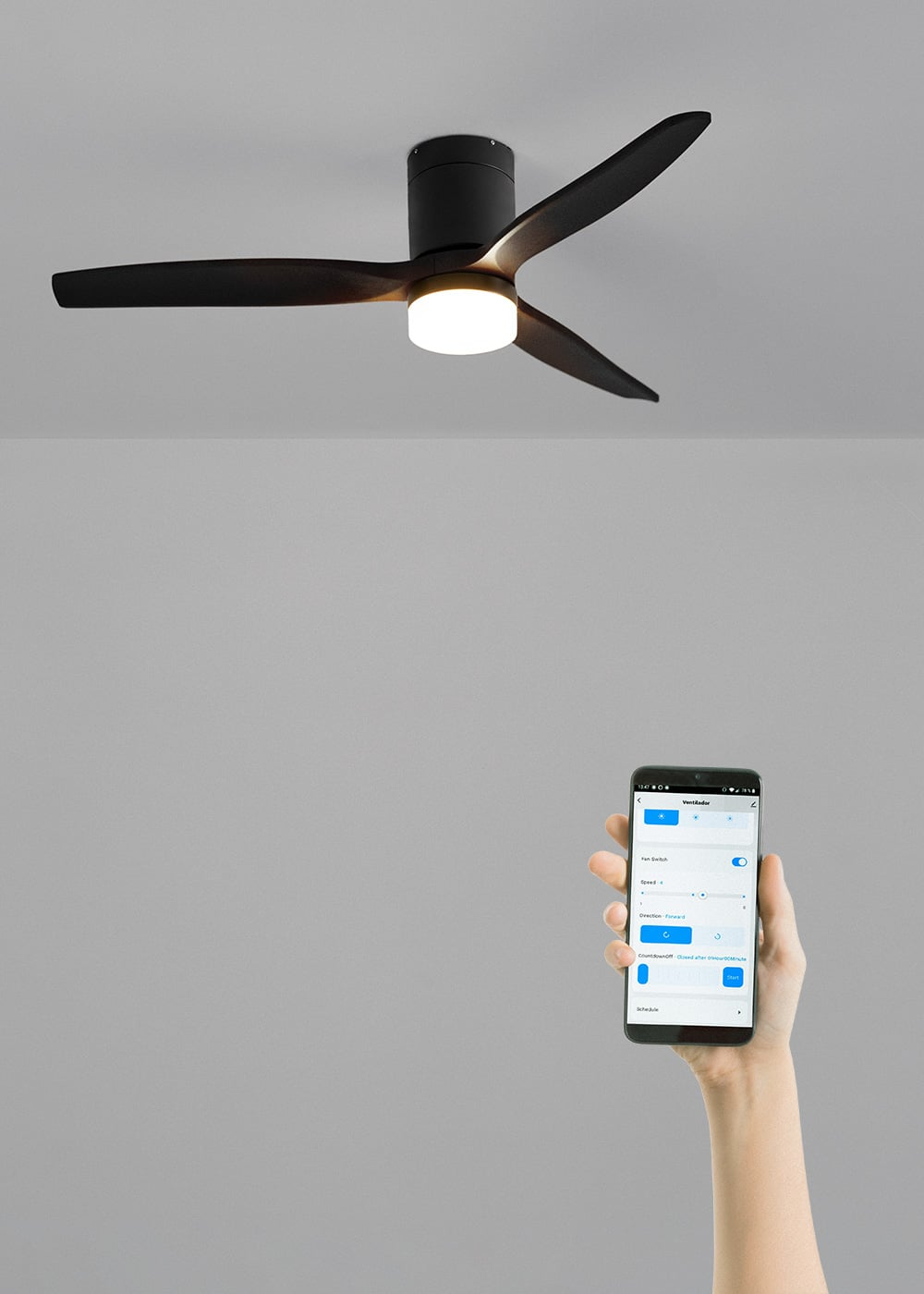 Un ventilador de techo negro con luz está en el techo. Una mano sostiene un teléfono mostrando controles del ventilador.