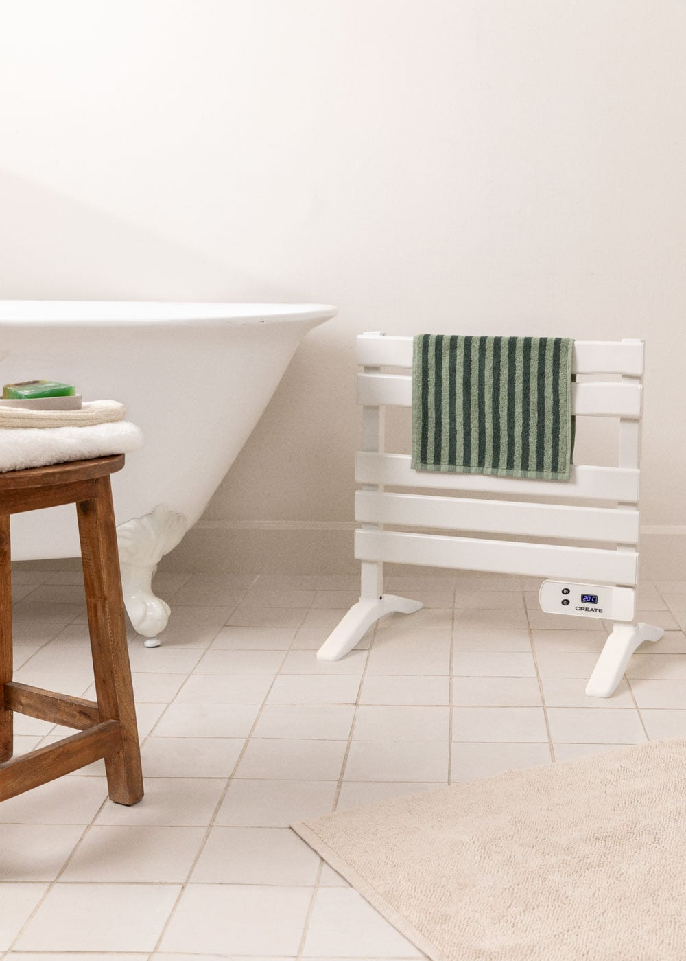Escena de baño con bañera exenta, taburete y toallero blanco con toalla a rayas.