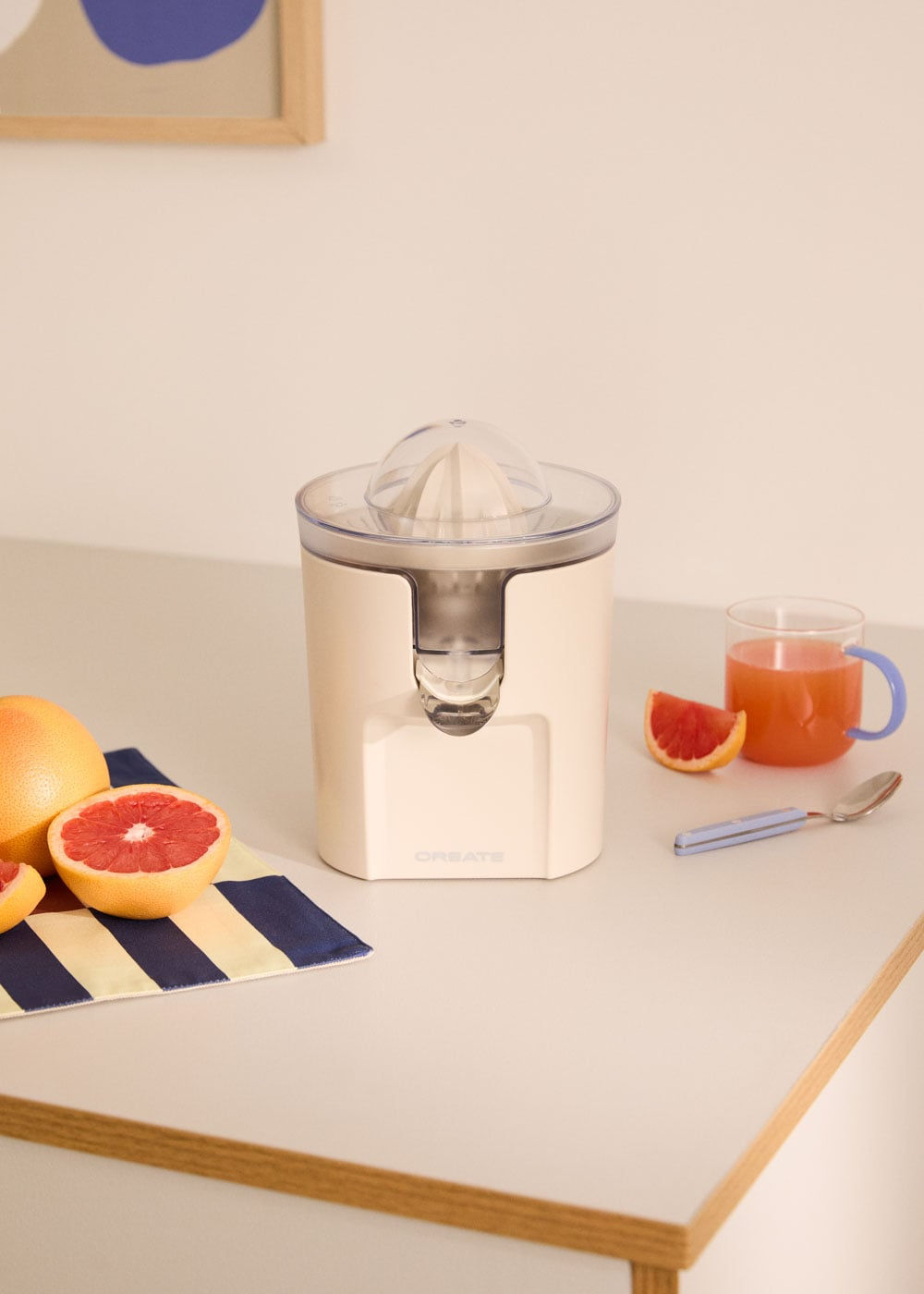 Un exprimidor de cítricos eléctrico beige con pomelos y zumo en una mesa.