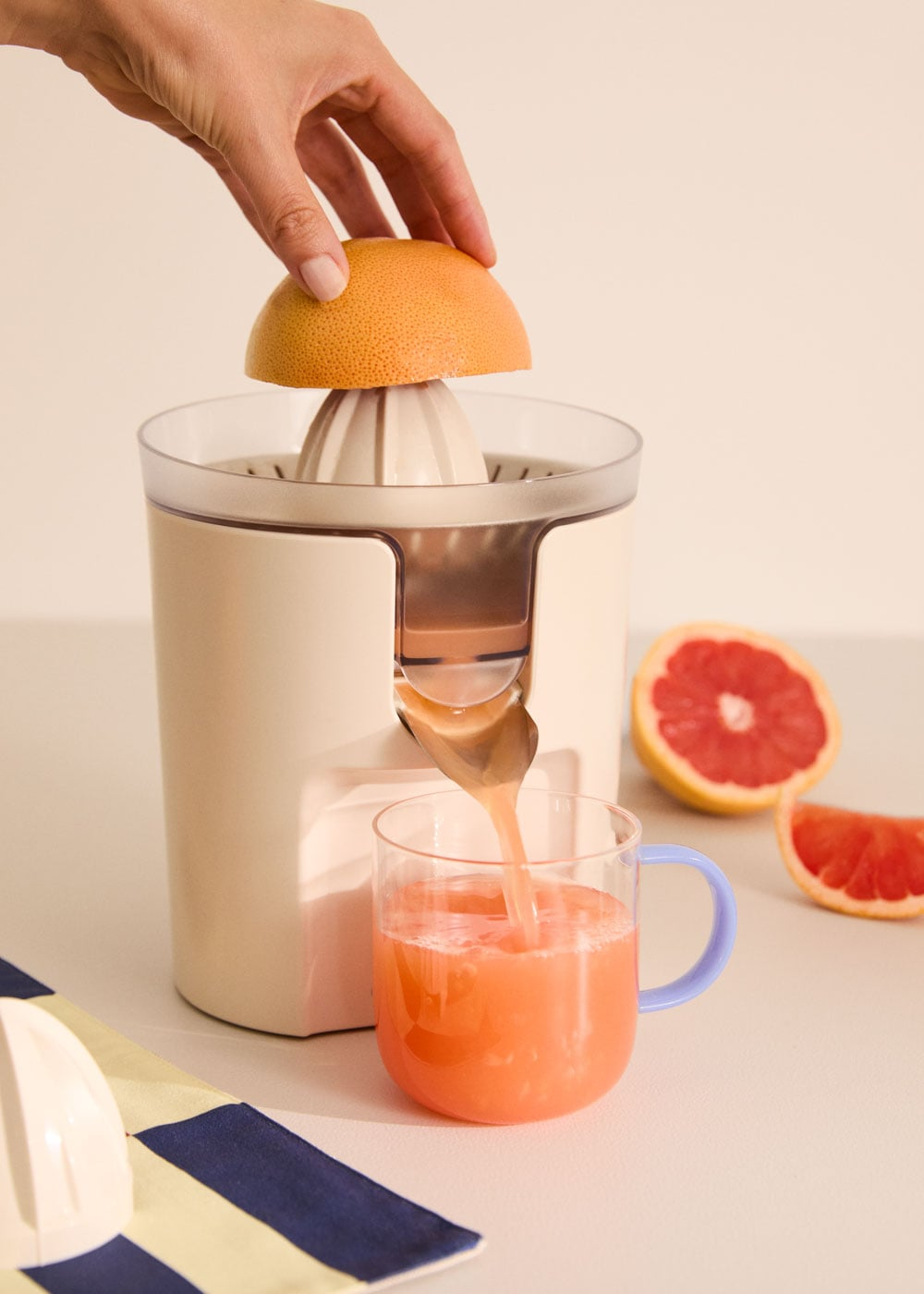 Una mano presiona una toronja en un exprimidor, el jugo fluye hacia un vaso.