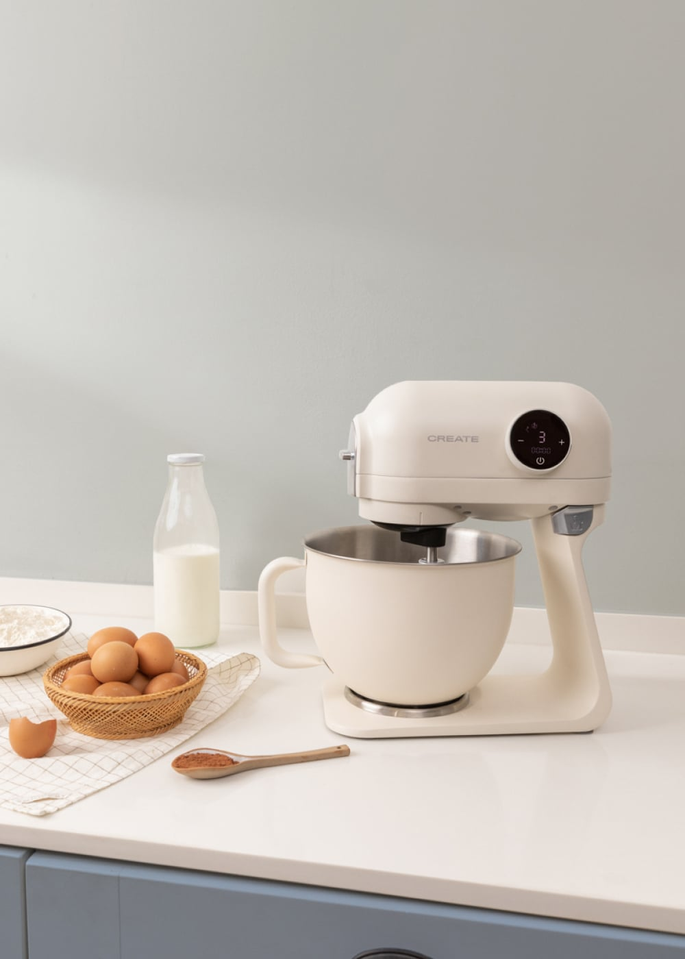 Un robot de cocina color crema con huevos, leche, harina y una cuchara de cacao.