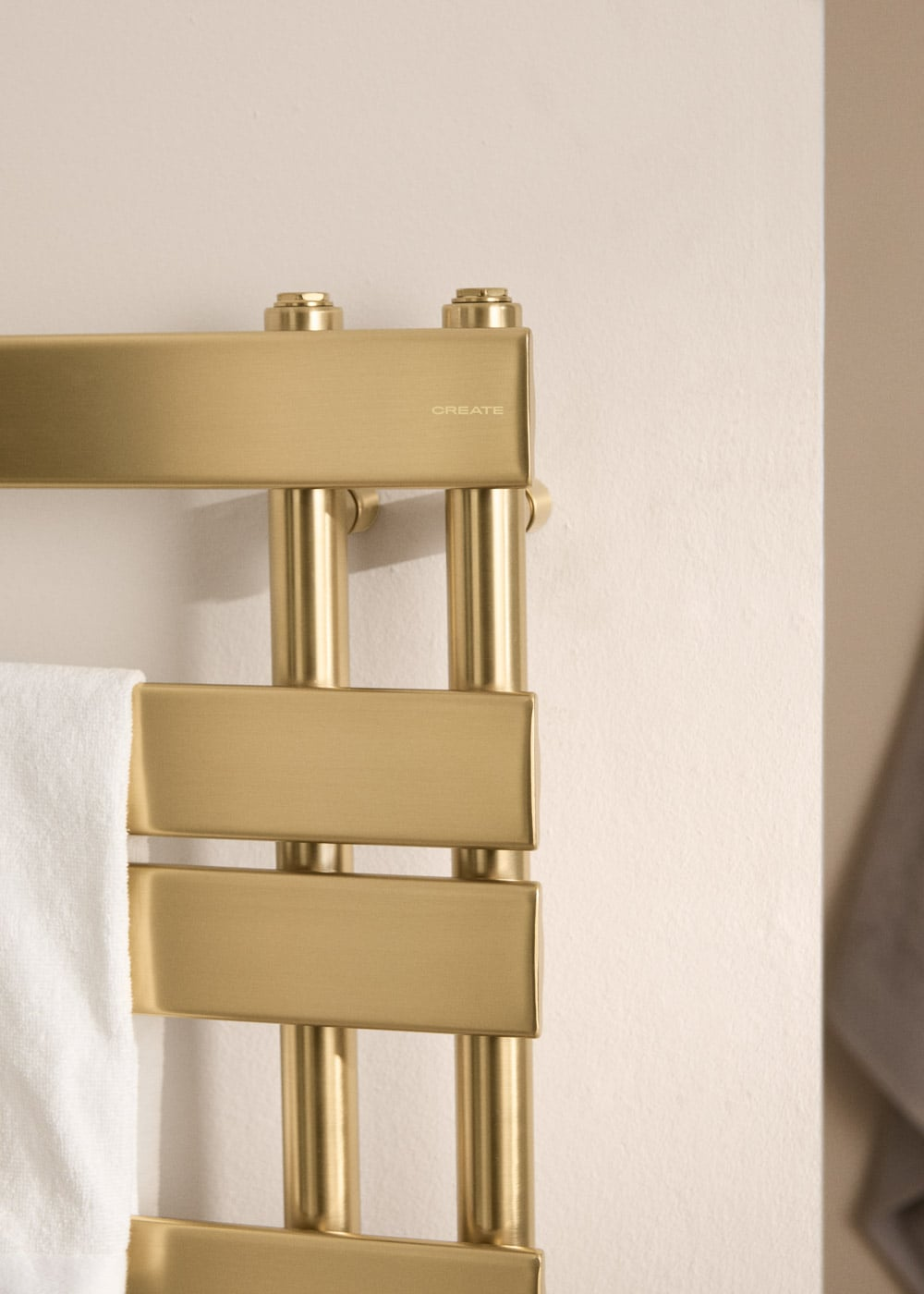 Un toallero dorado con una toalla blanca, montado en una pared color crema.