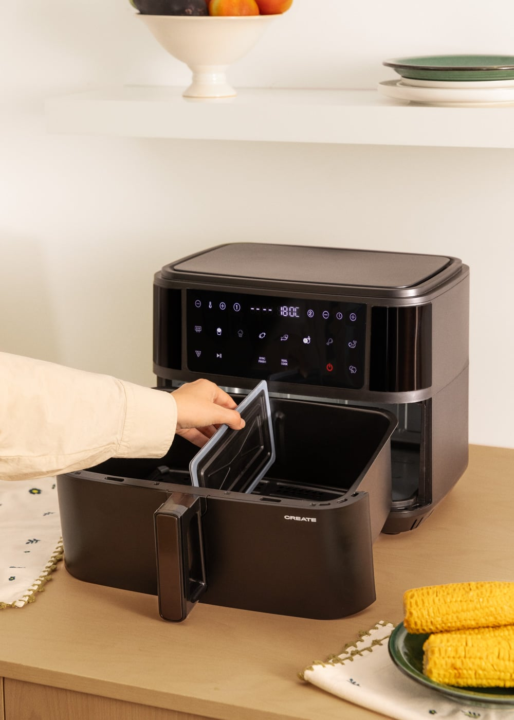 Une main place un séparateur dans une friteuse à air noire ouverte avec écran numérique.