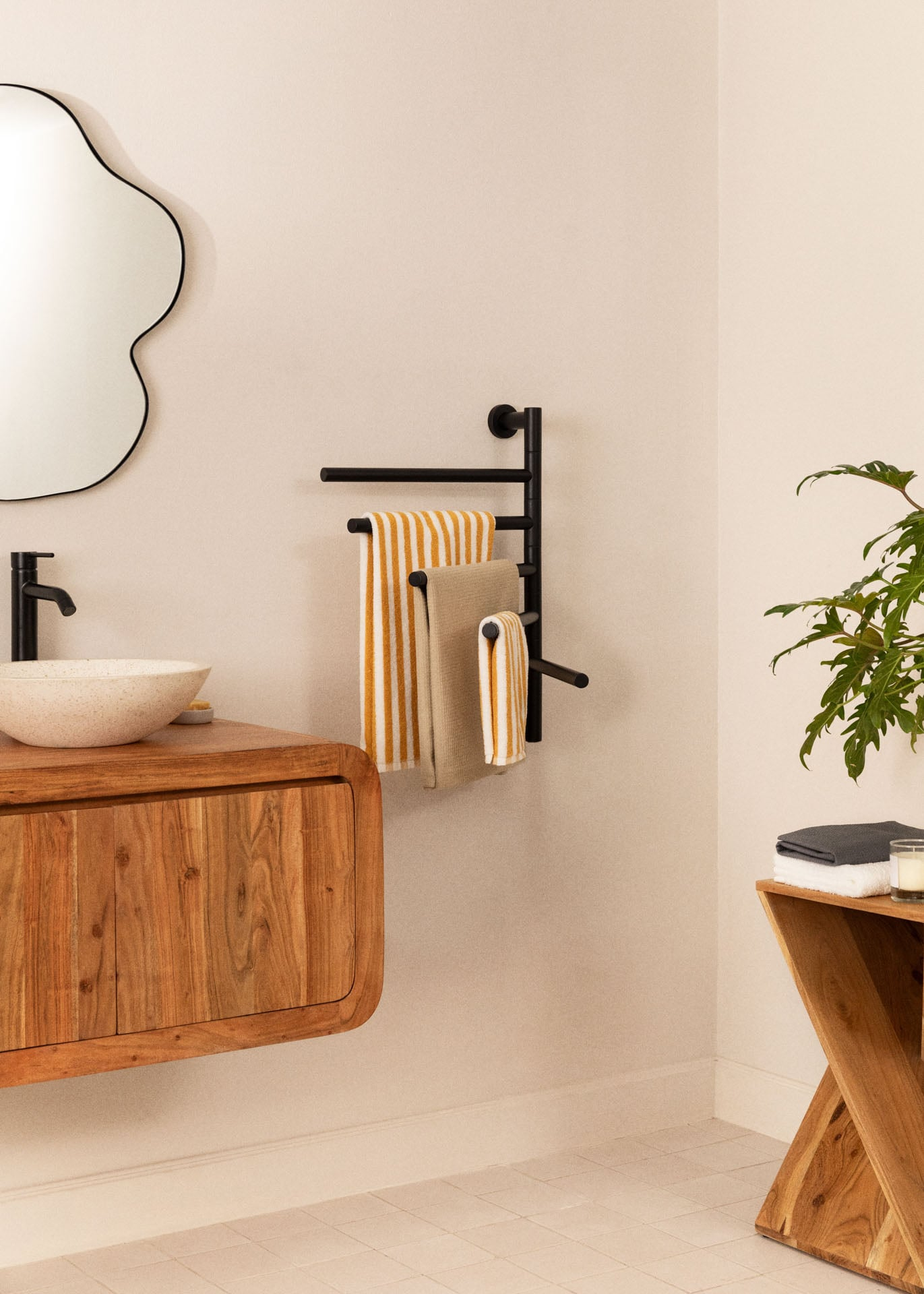 Un baño moderno con tocador de madera, lavabo, toallero negro con toallas y una planta.
