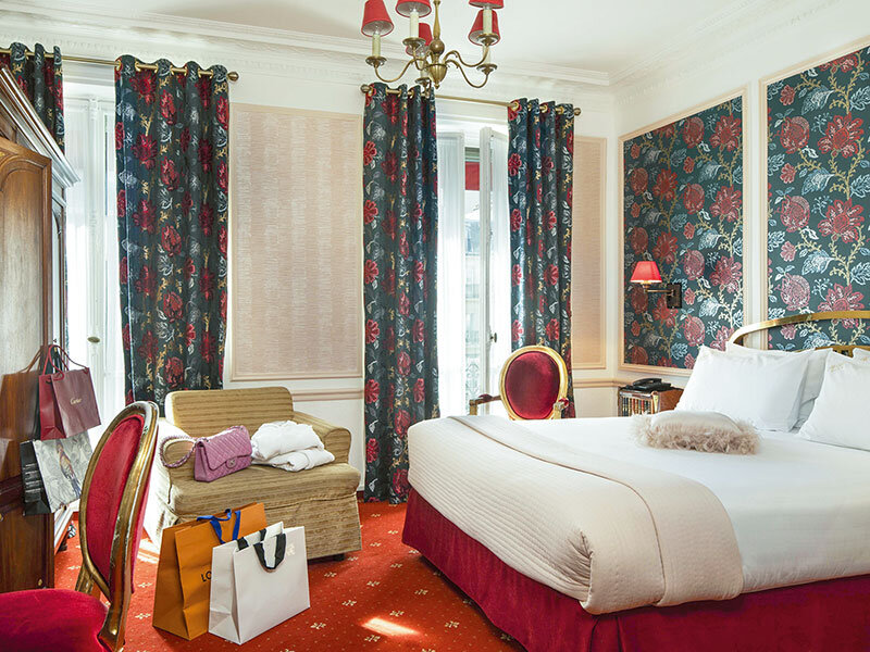 Una lujosa habitación de hotel con cama, sillón, cortinas y bolsas de compras.