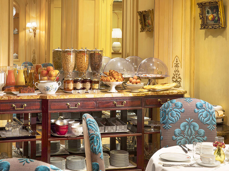 Buffet con jugos, frutas, cereales, pasteles, huevos y pan en una sala elegante.