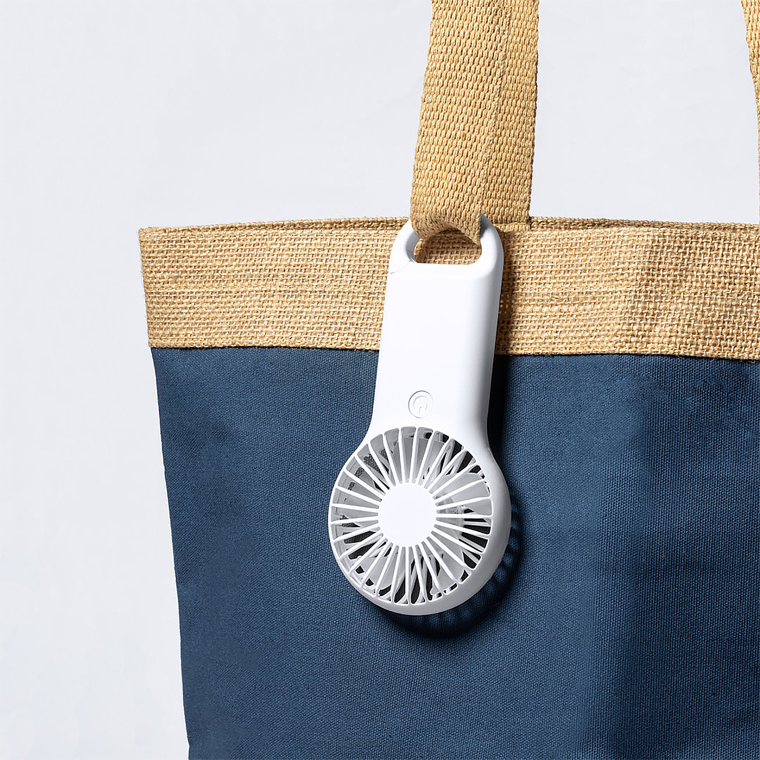 Un mini ventilador blanco está sujeto a una bolsa de mano con asas de yute.