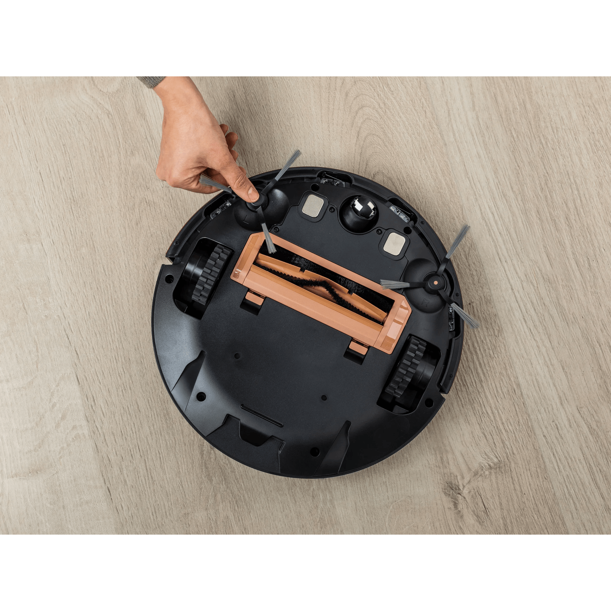 Mano toca cepillo de aspiradora robot negra en suelo de madera.