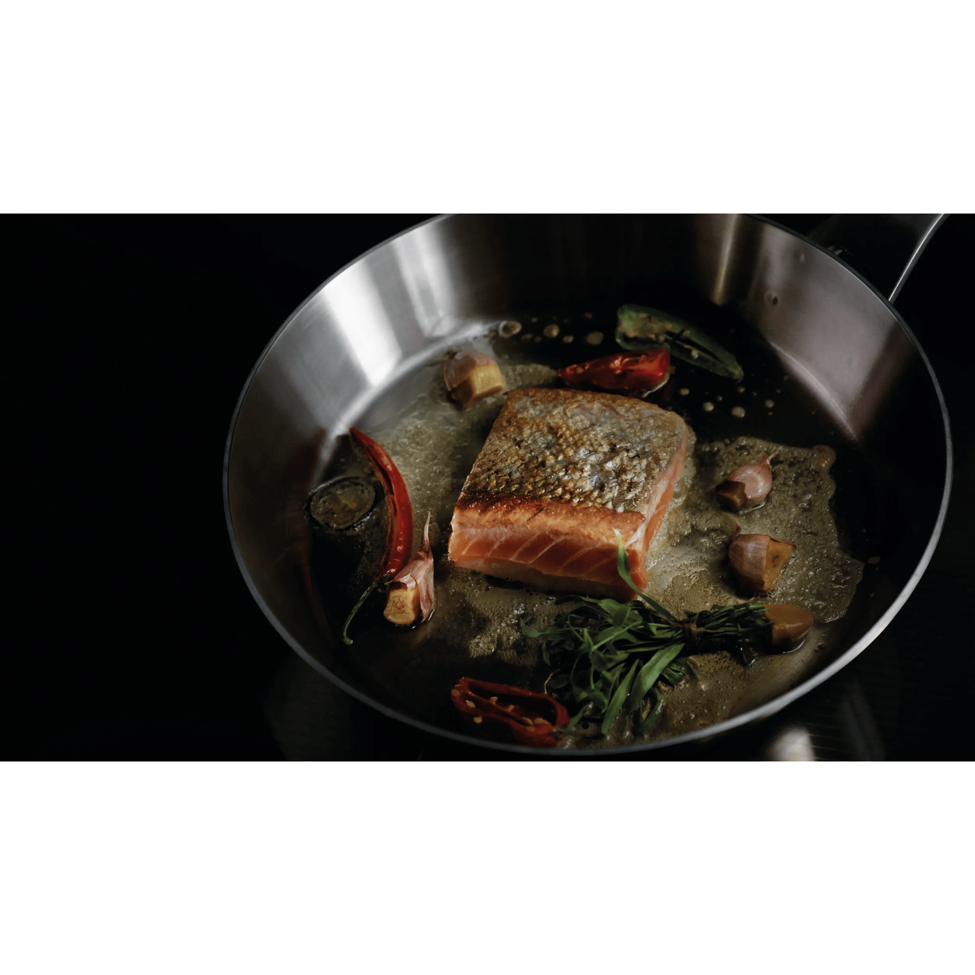 Filete de salmón friéndose en sartén con chile, ajo y hierbas.