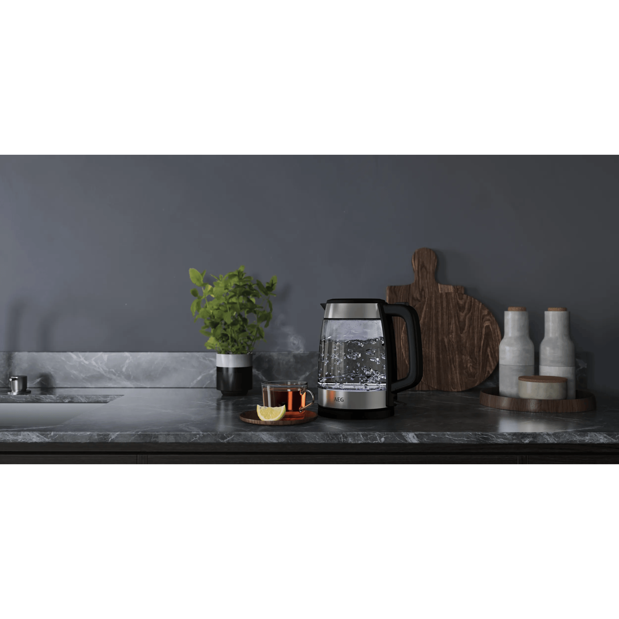 Ein Glaswasserkocher kocht Wasser, daneben eine Tasse Tee mit Zitrone.