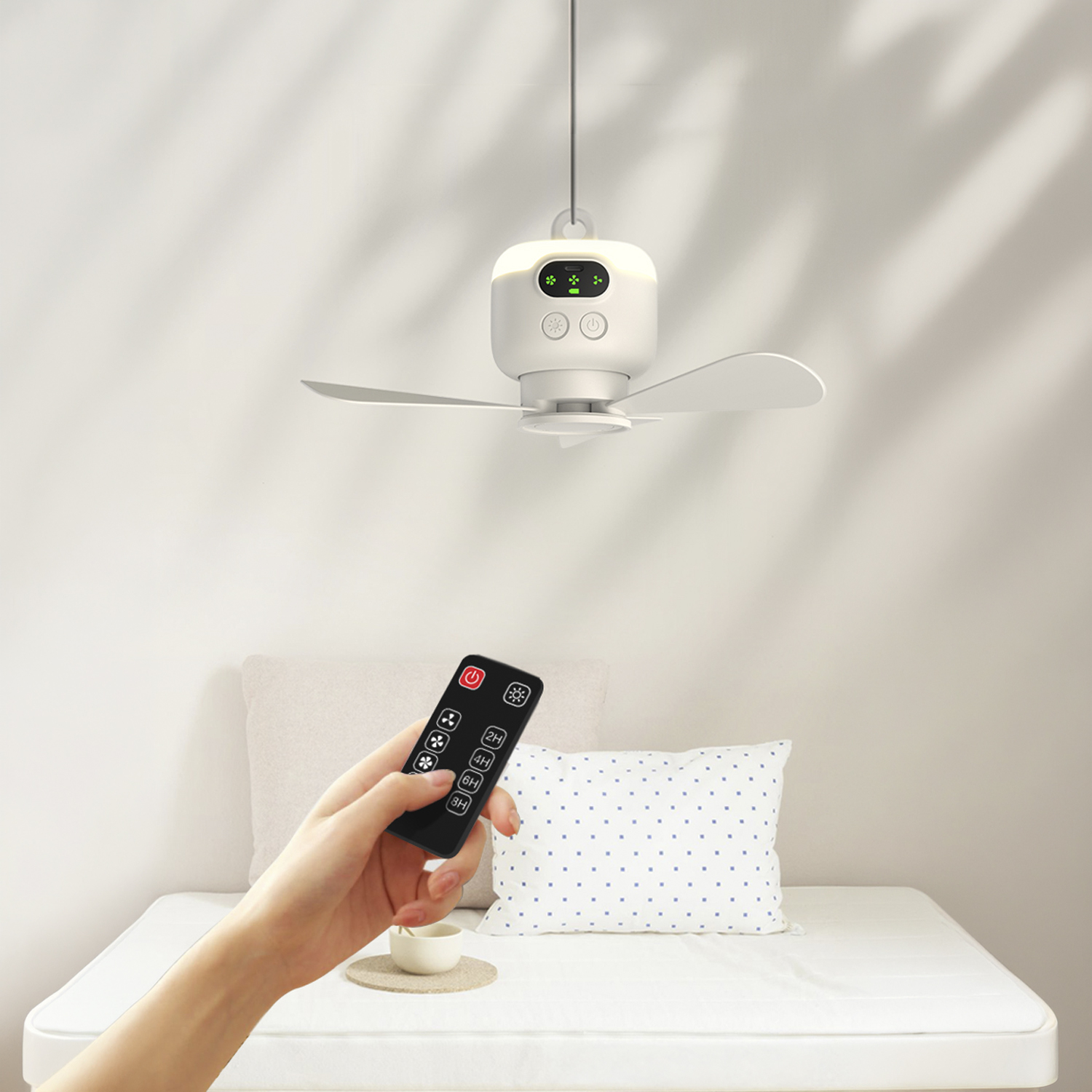 Una mano sostiene un control remoto para un ventilador de techo blanco con luz e indicadores verdes.