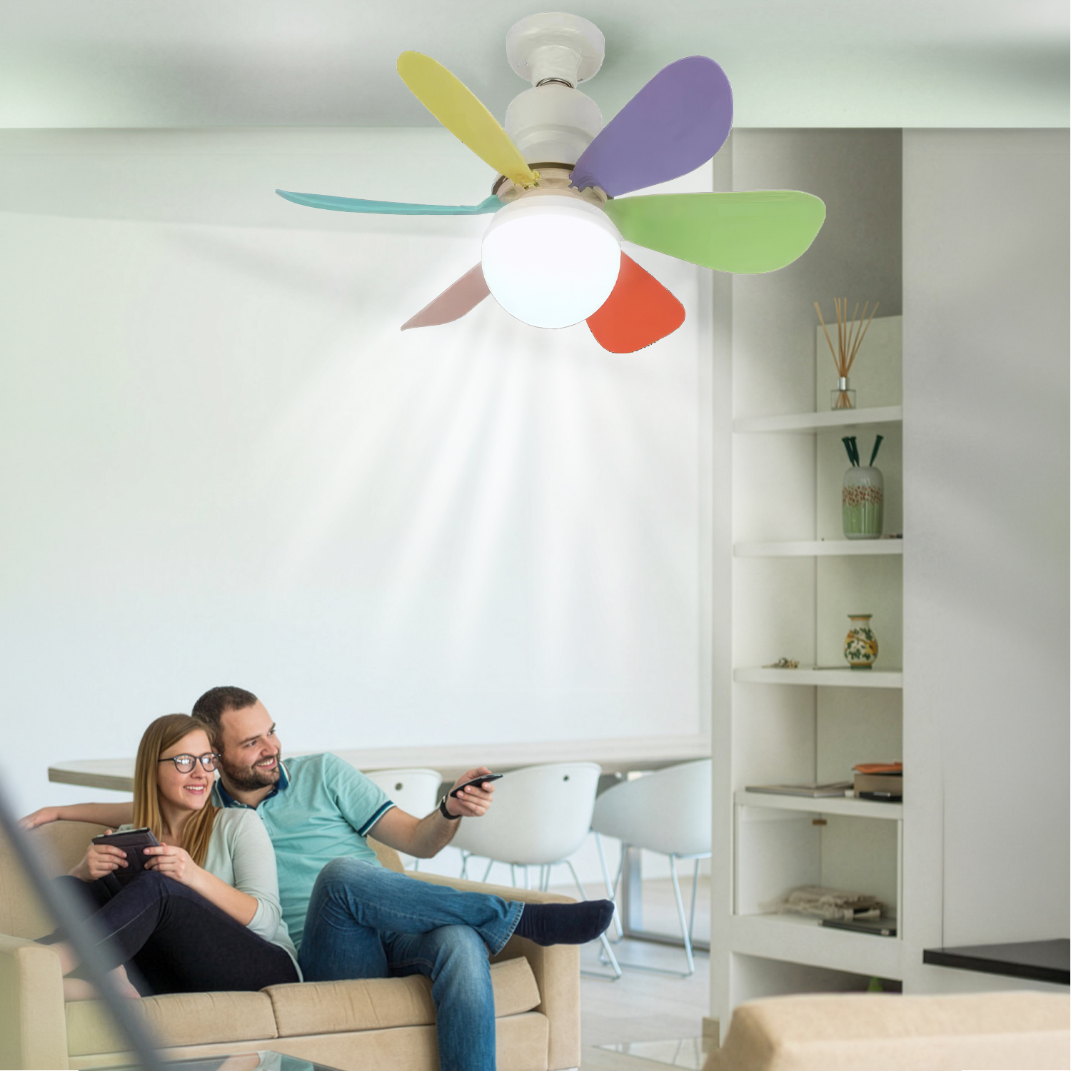 Una pareja relajándose en un sofá con un ventilador de techo de aspas coloridas encima.