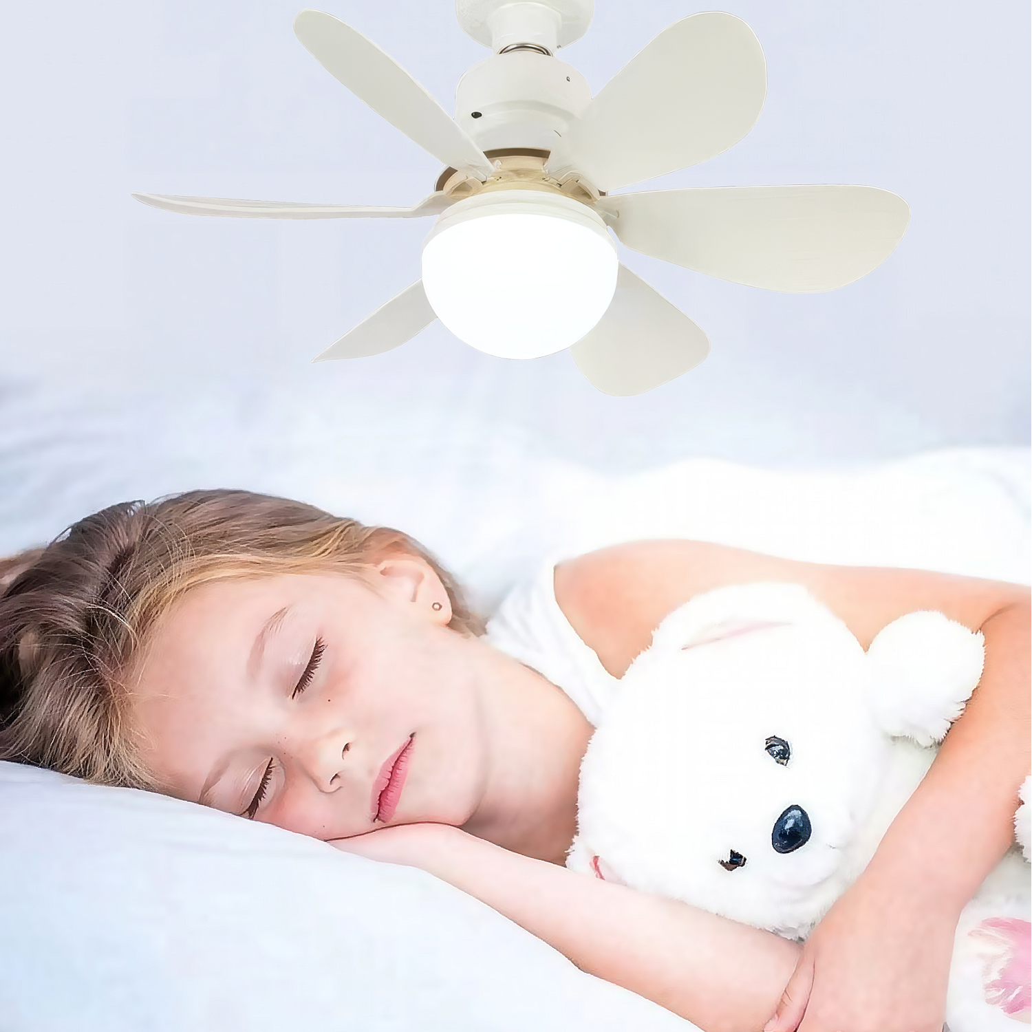Una niña duerme con un osito de peluche bajo un ventilador de techo.
