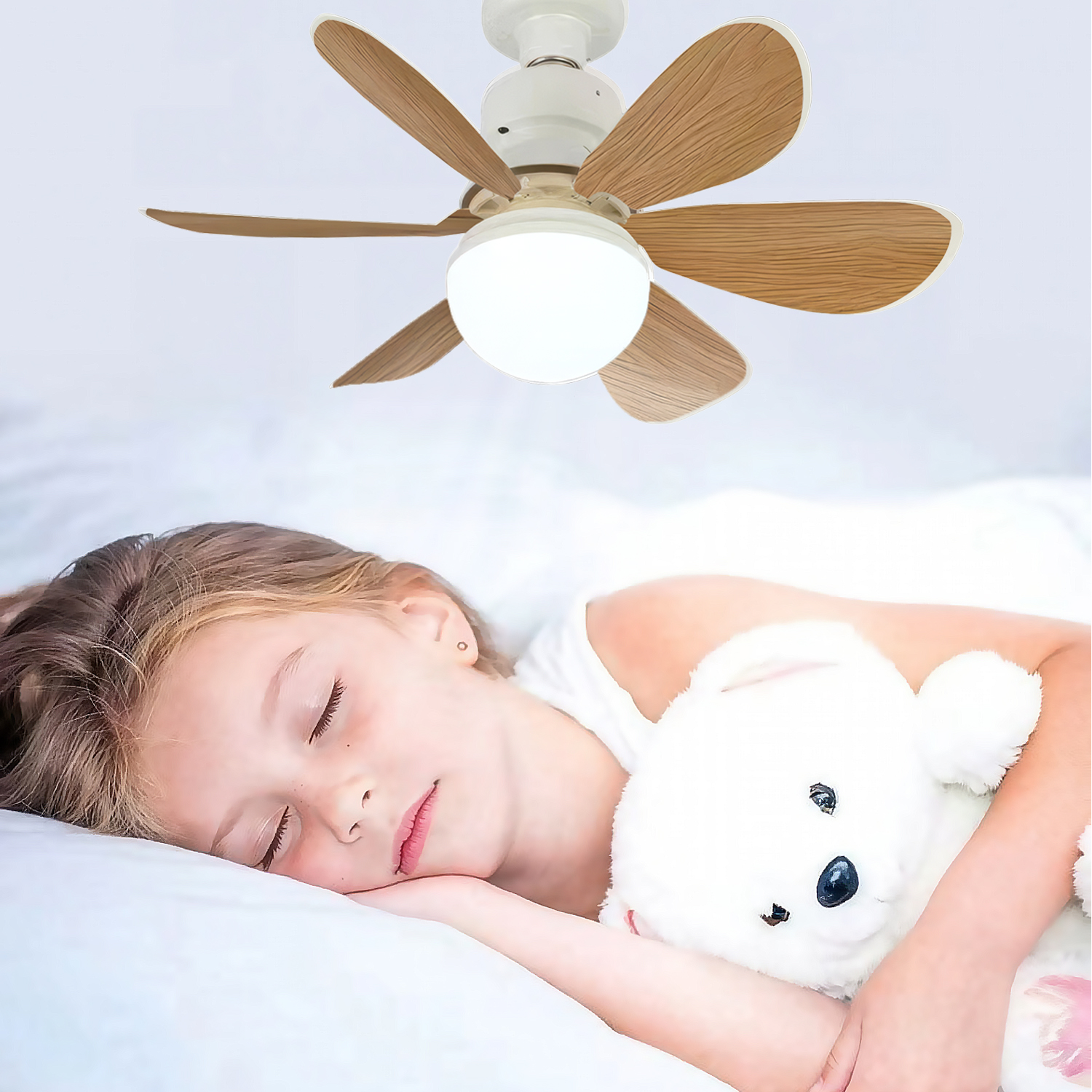 Una niña duerme plácidamente con un osito de peluche bajo un ventilador de techo.