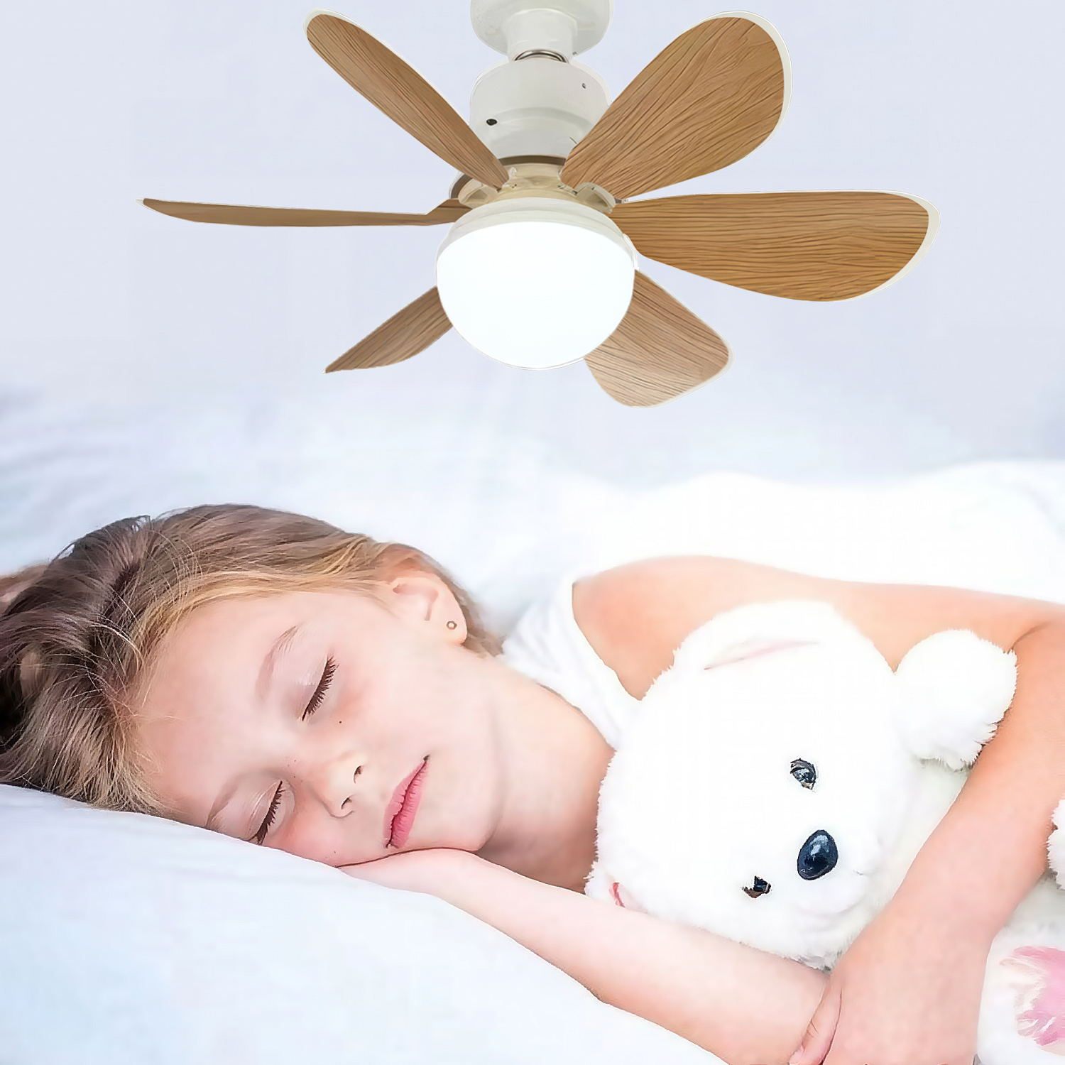Una niña duerme plácidamente en la cama, abrazando un osito de peluche blanco. Un ventilador de techo está arriba.