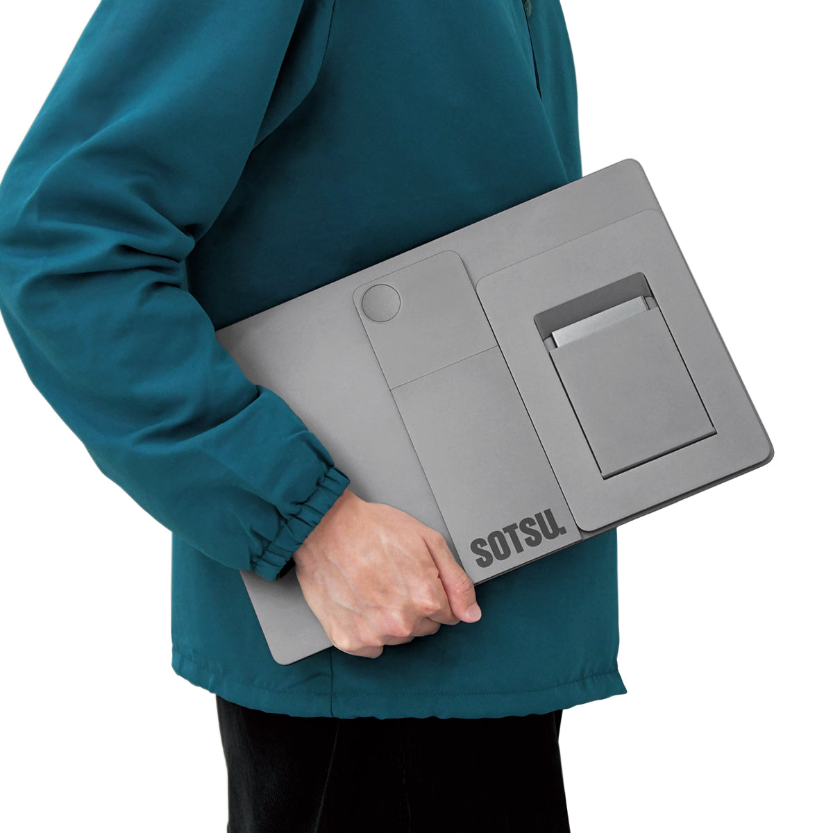 Osoba w turkusowej kurtce trzyma szarą podstawkę pod laptopa.
