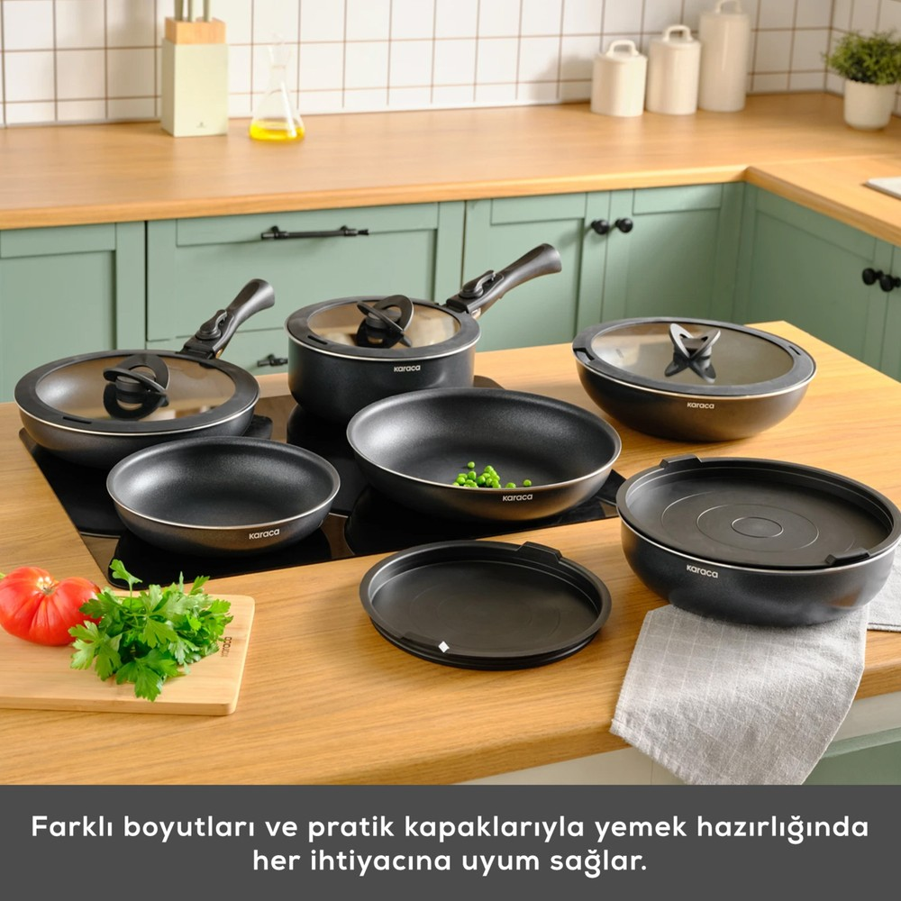 Siyah tencere ve tava seti, cam kapaklı, ahşap tezgah üzerinde.