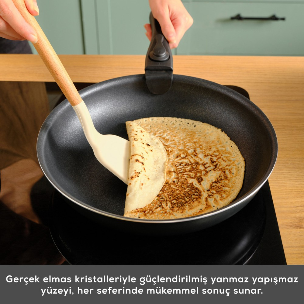 Bir kişi spatulayla tavada bir krep çeviriyor.