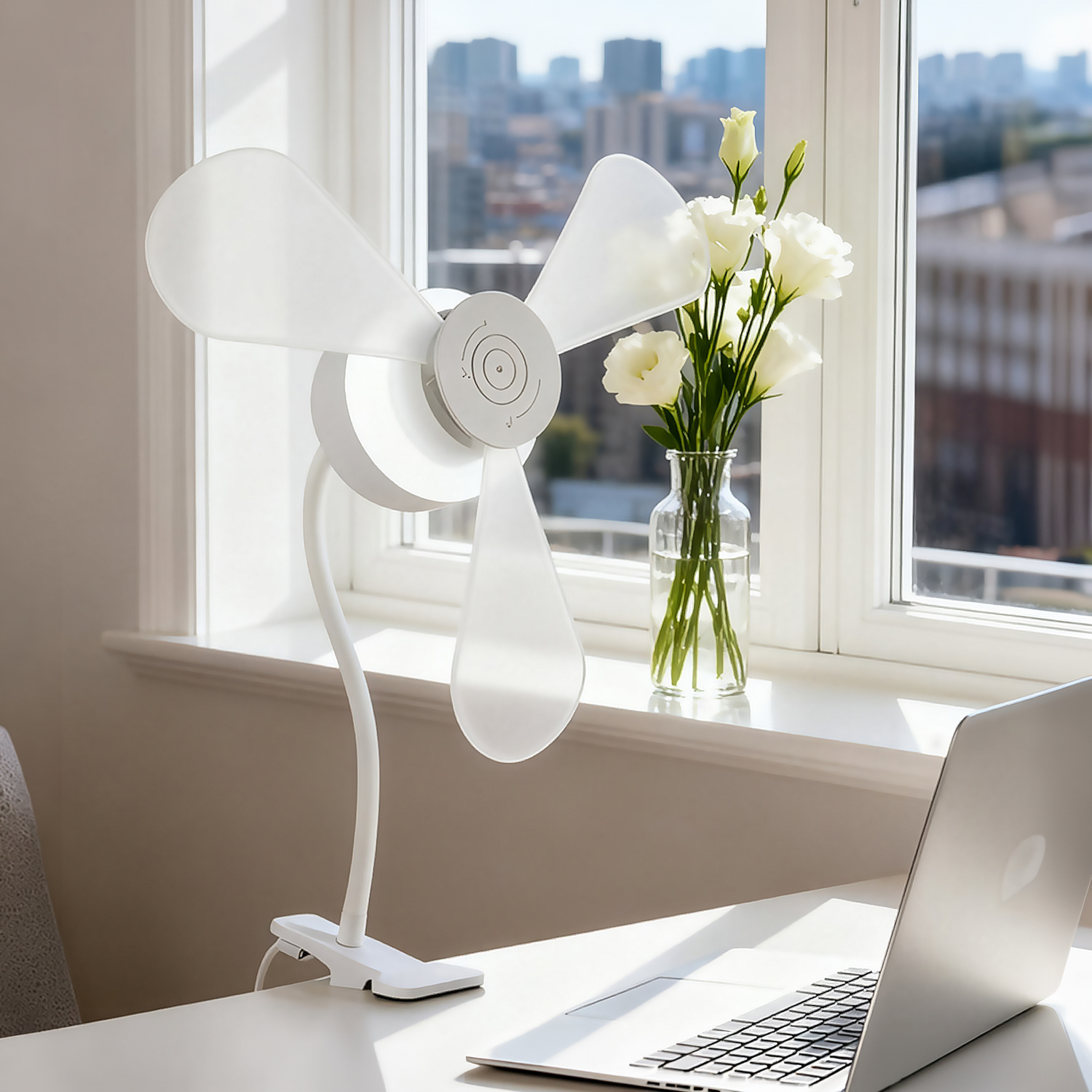 Un ventilador blanco junto a flores en una mesa con portátil.
