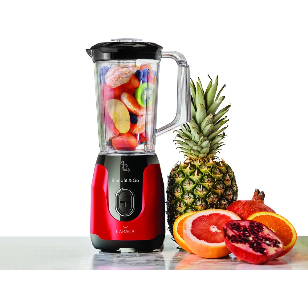 İçinde meyve olan kırmızı bir blender, ananas, nar ve narenciye meyvelerinin yanında duruyor.