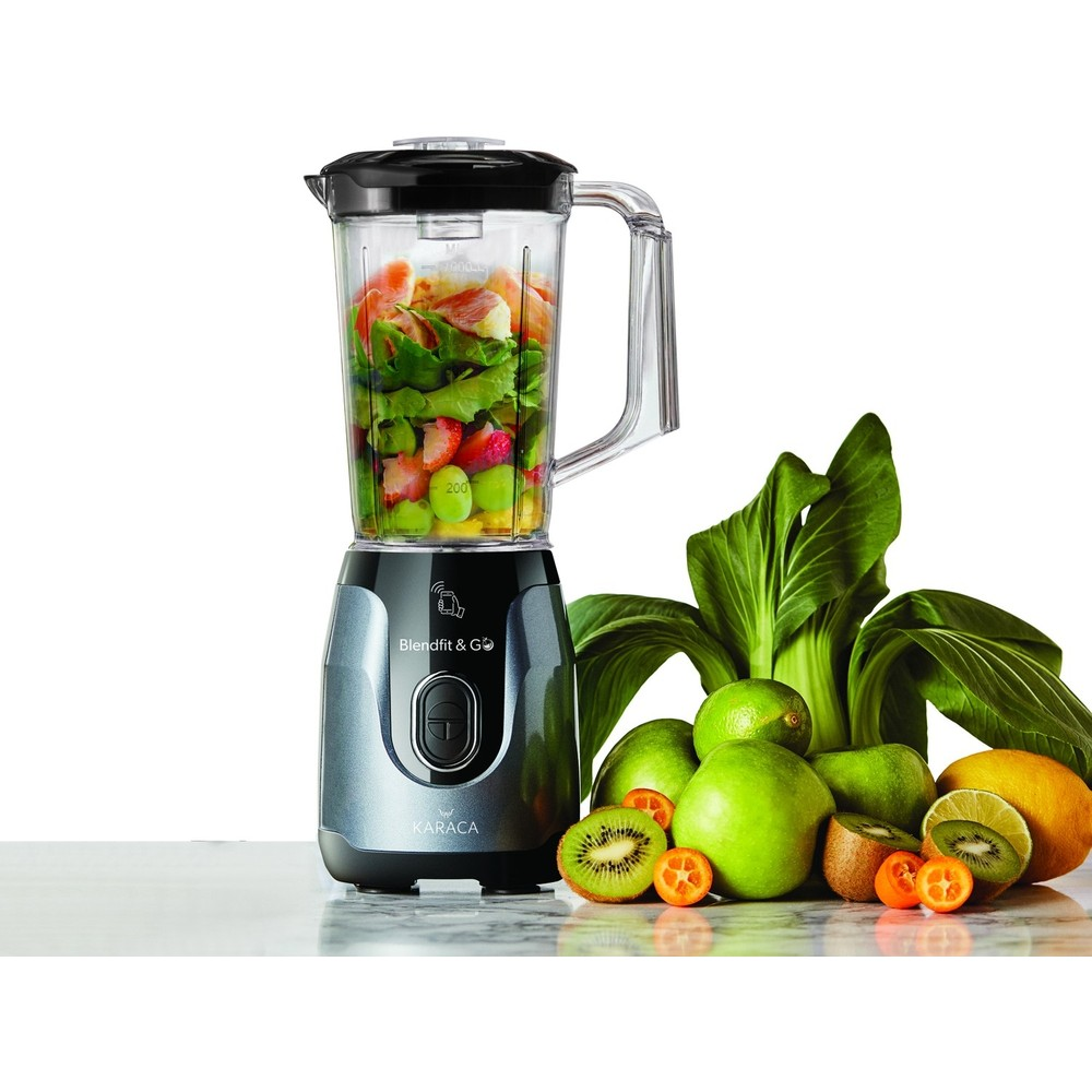 Meyve ve yeşillikle dolu blender, taze meyve ve sebzelerin yanında duruyor.