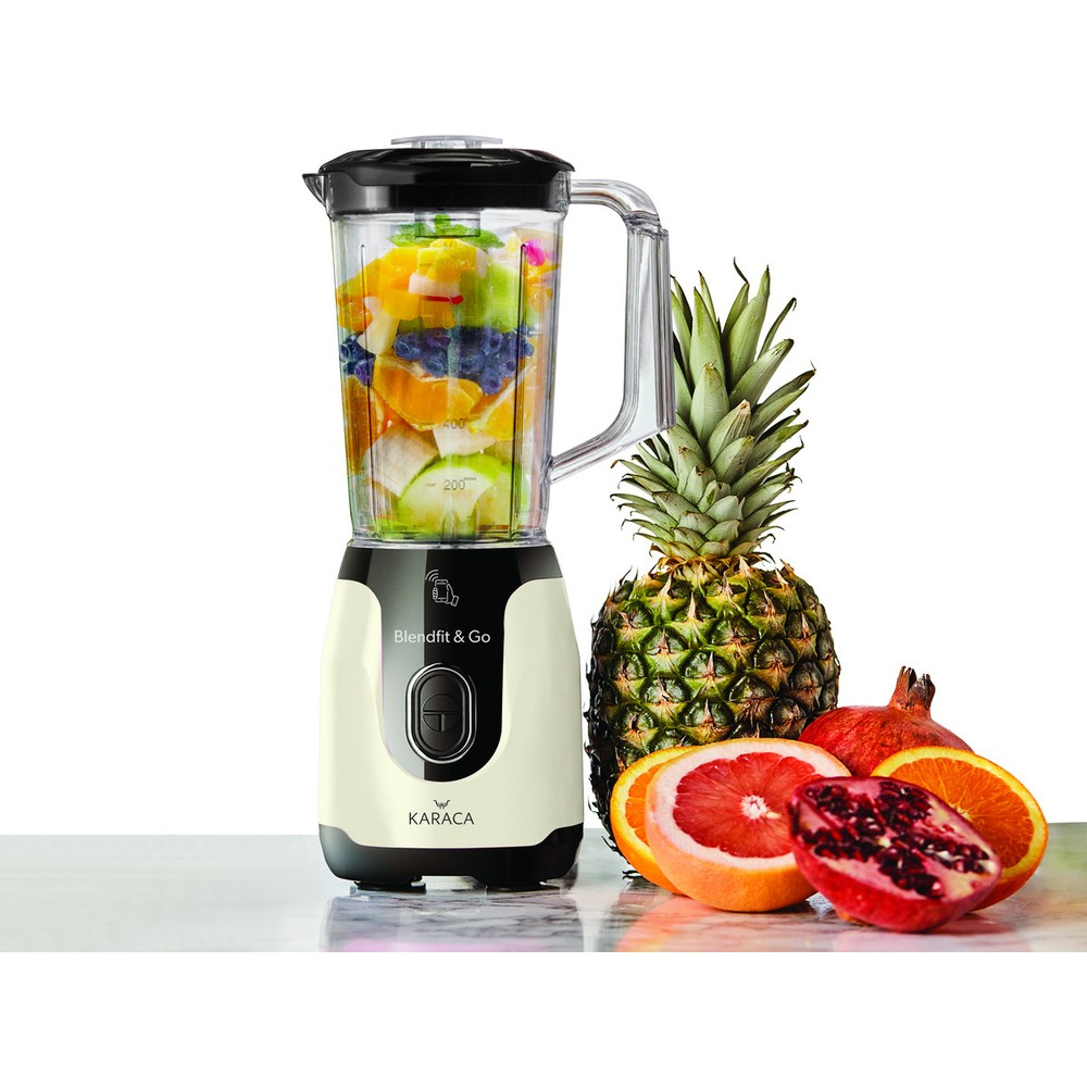 İçinde meyveler olan krem ve siyah blender, ananas, nar ve portakalların yanında.